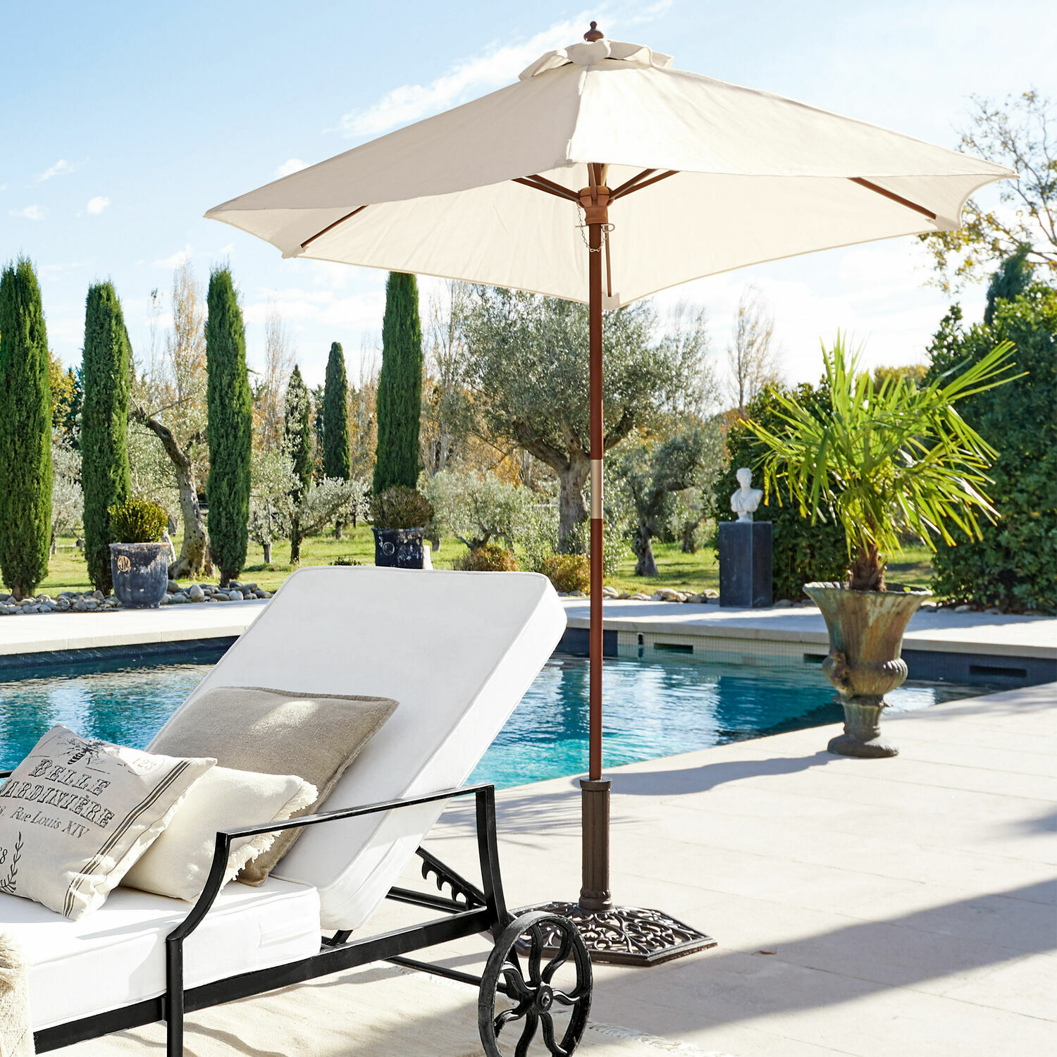 Weißes Liegestuhl mit Kissen und cremefarbener Gartenschirm neben Pool auf Terrasse