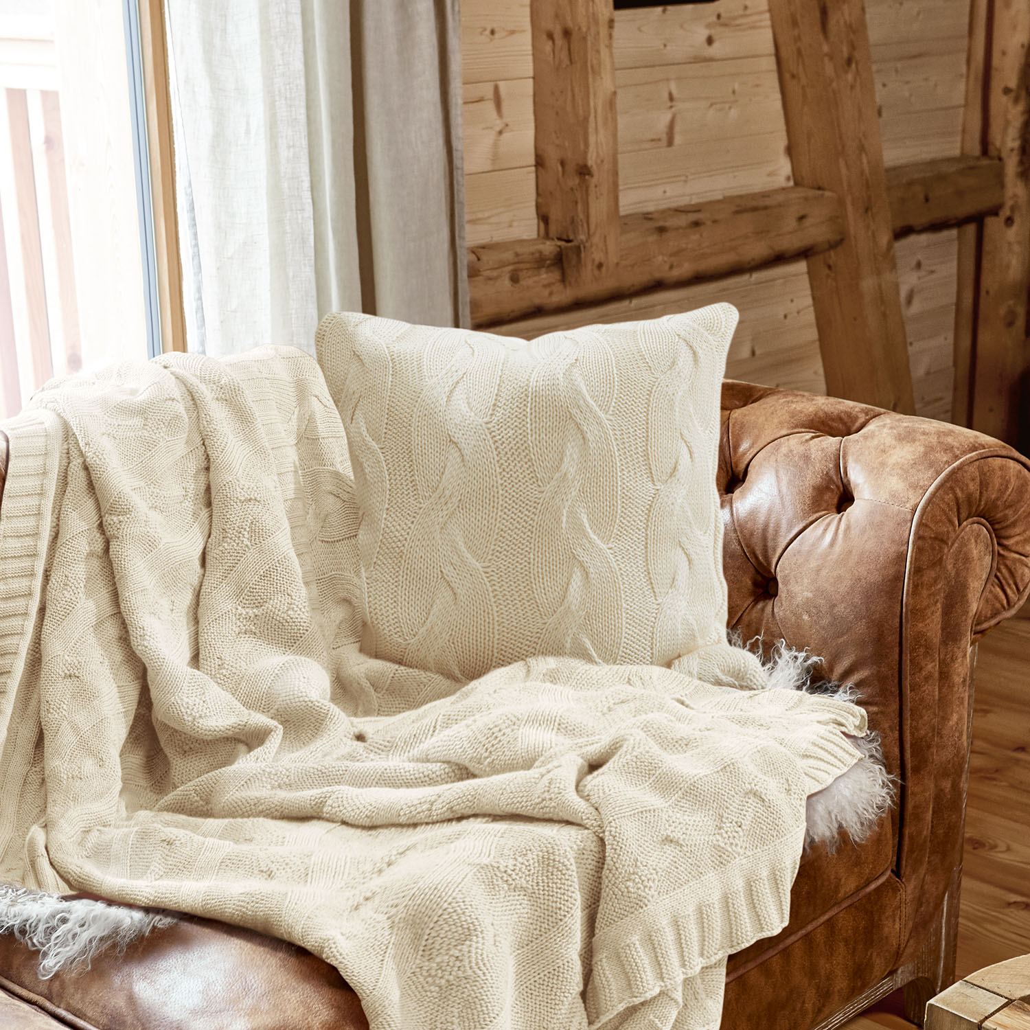 Beige gestrickte Decke und Kissen mit Zopfmuster auf braunem Ledersofa in Holzraum