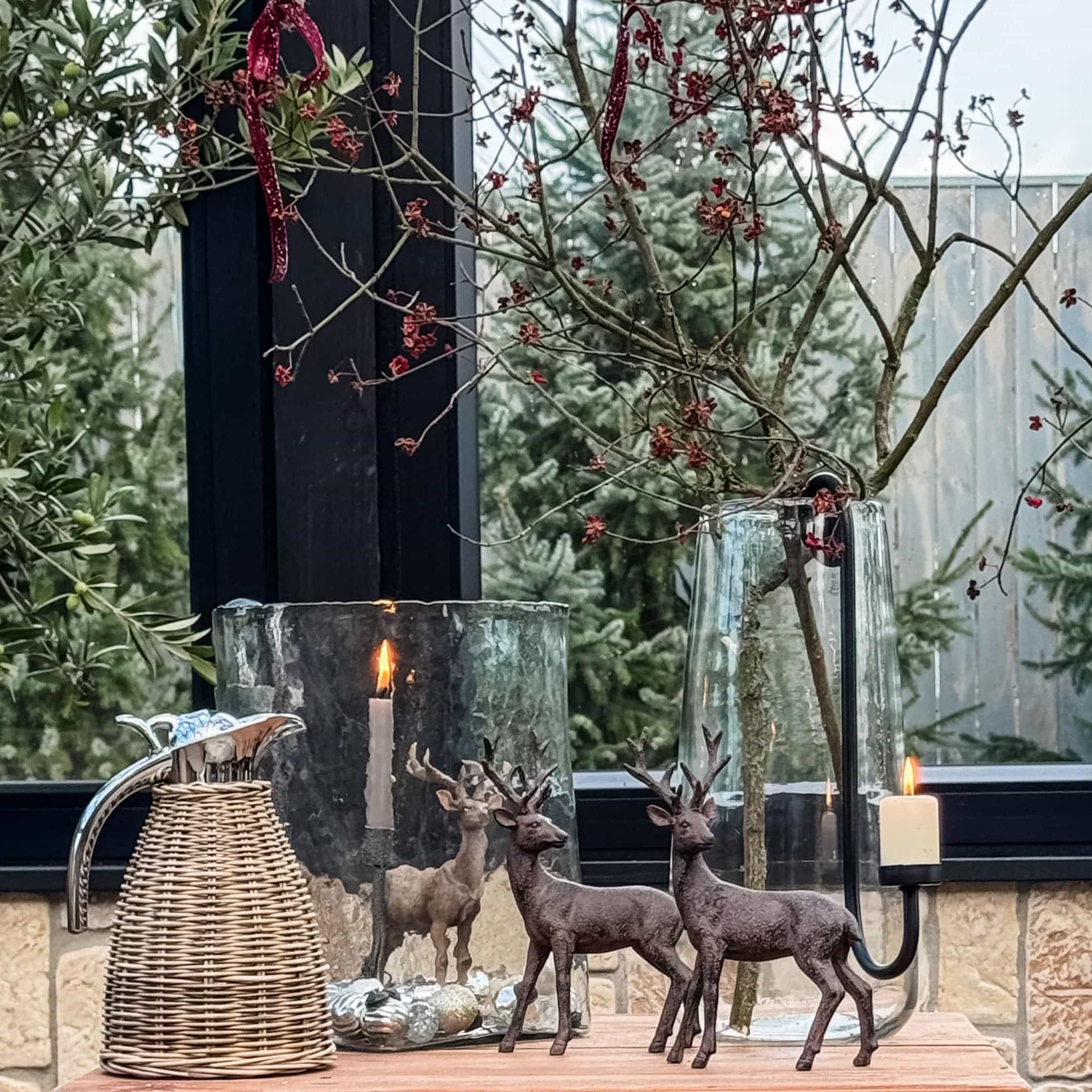 Weihnachtliche Dekoration mit zwei braunen Hirschfiguren, Glaswindlicht und Rattankrug auf Holztisch