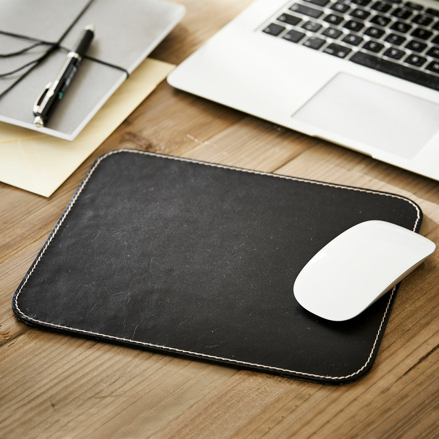 Schwarze Leder-Mausunterlage mit weißer Naht auf Holztisch neben Laptop