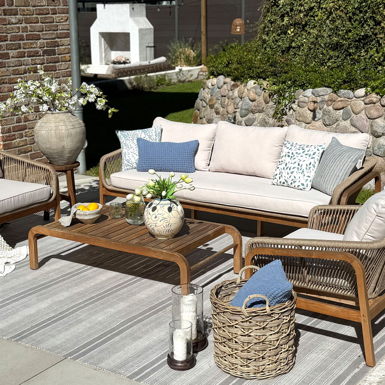 Gartenmöbel-Set mit Holztisch und beigem Sofa mit Kissen, Dekoration auf sonniger Terrasse