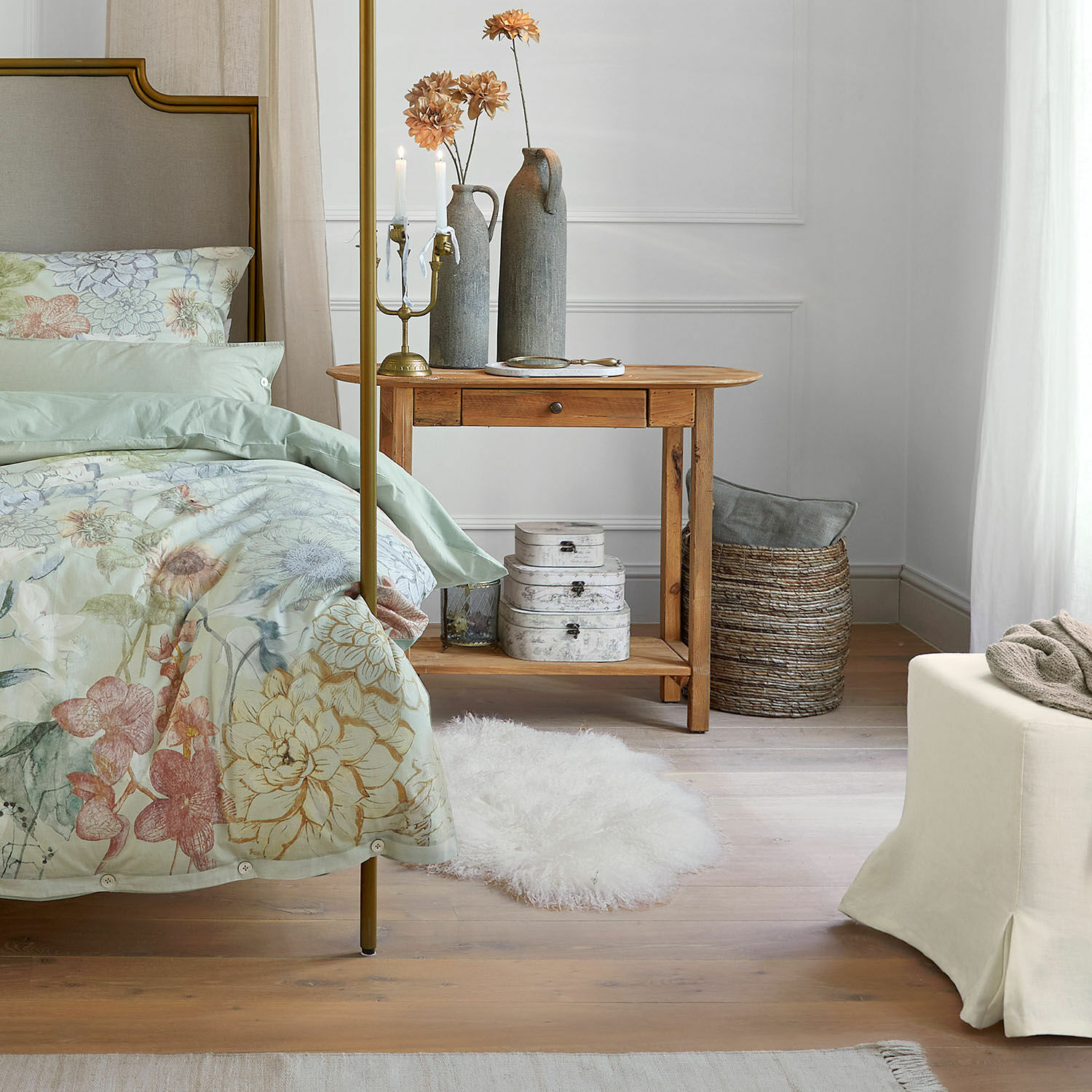 Schlafzimmer mit Holznachttisch, pastellfarbener Bettwäsche mit Blumenmuster und weichem weißem Teppich auf dem Boden