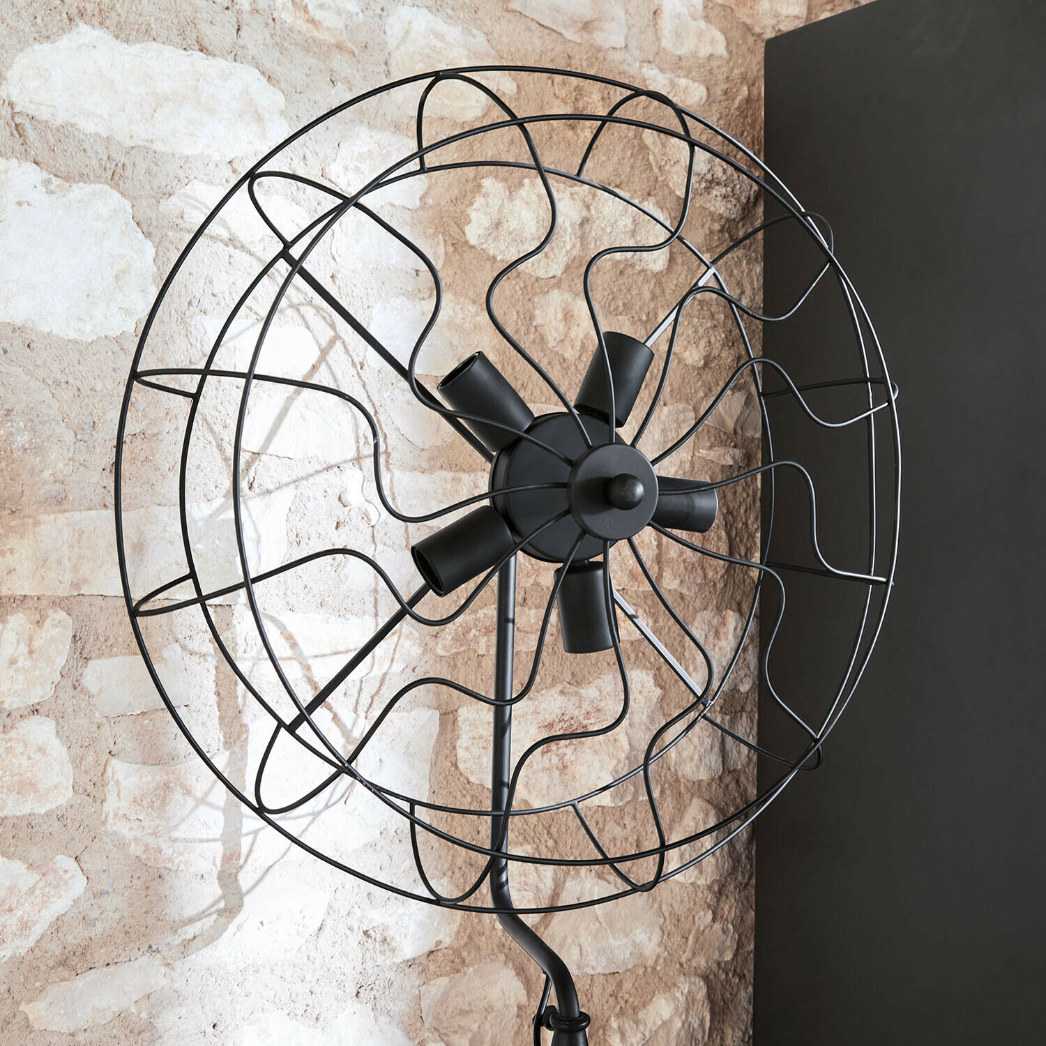 Schwarzer Metall-Standventilator mit dekorativem Gitter vor Steinwand, moderner Stil