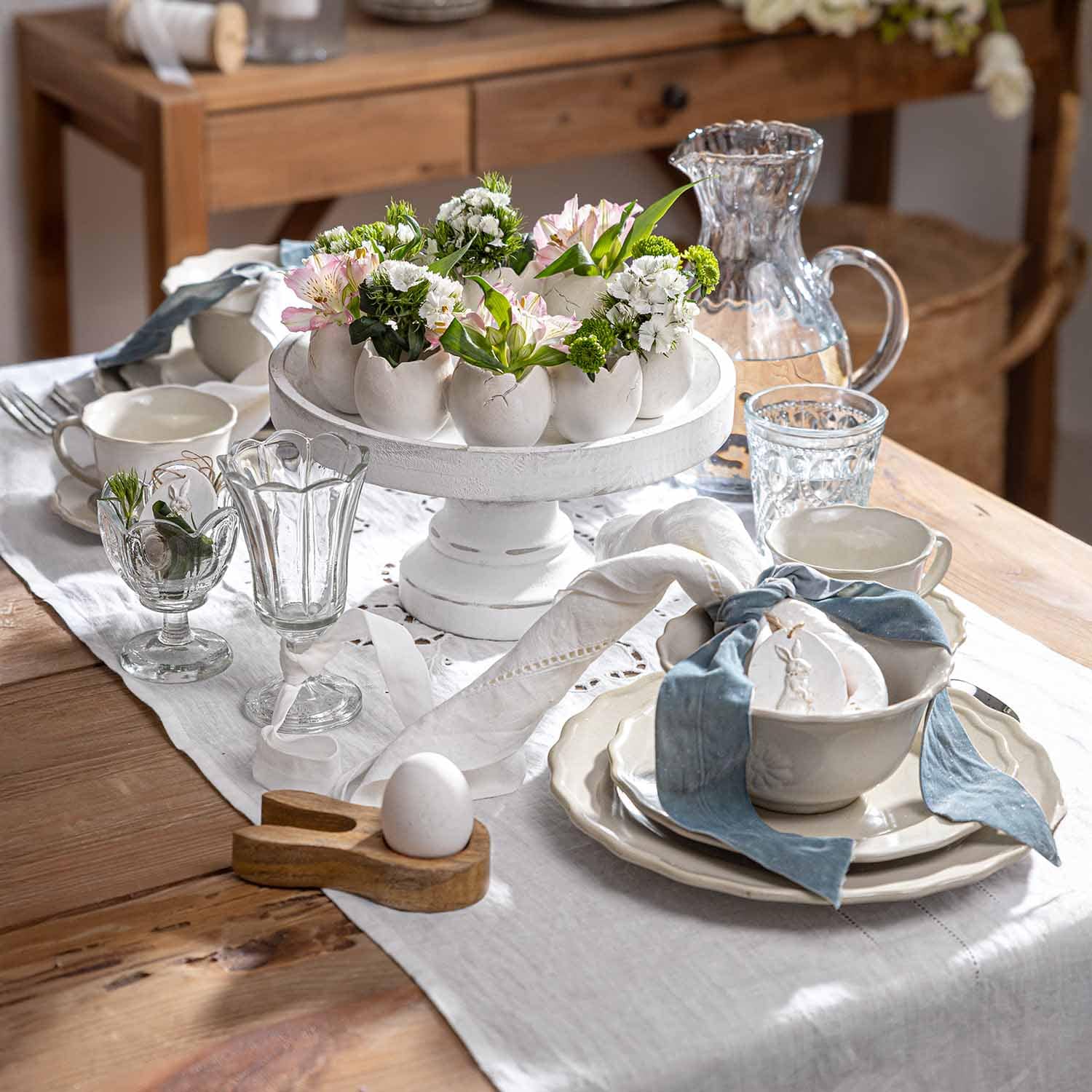 Weißer Keramikständer mit eiförmigen Blumentöpfen und Blumen auf rustikalem Holztisch dekoriert