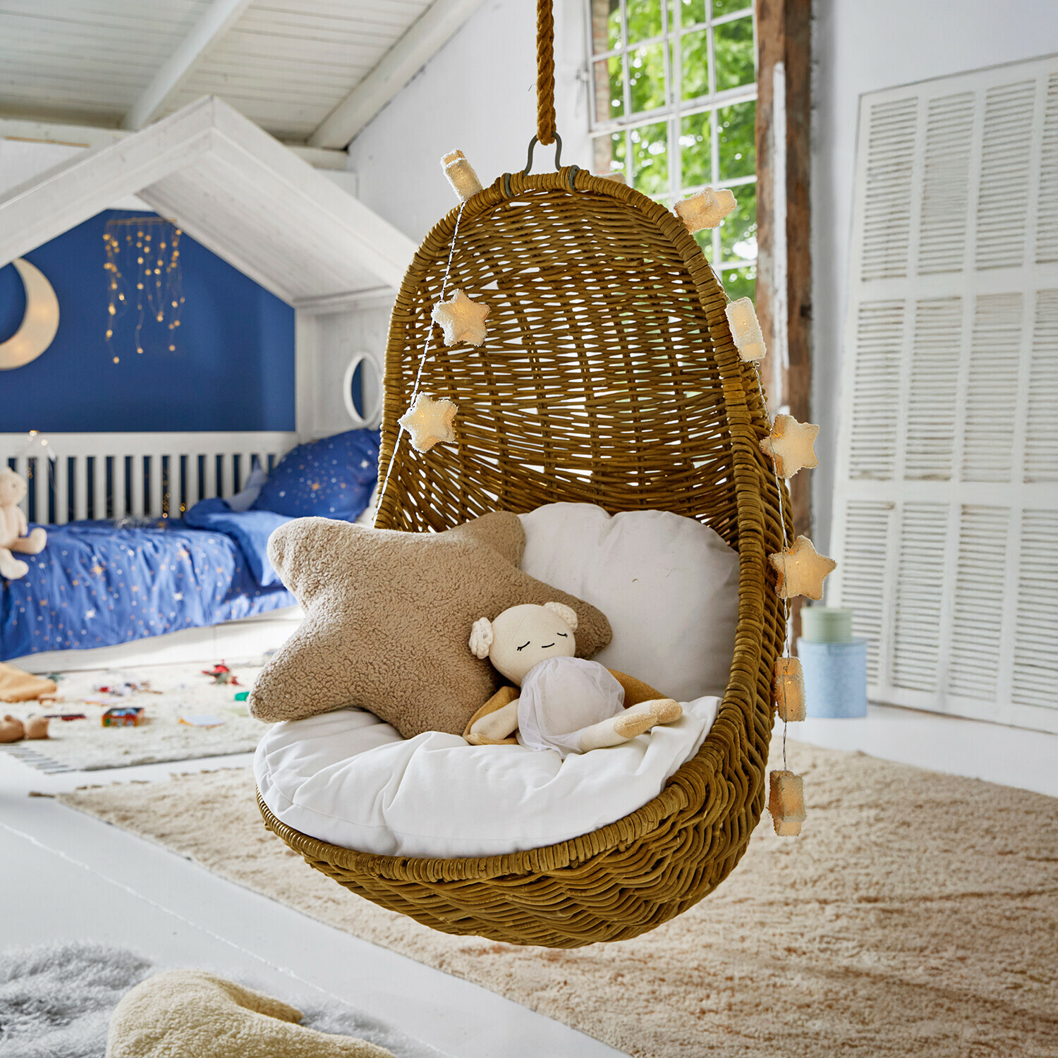 Hängesessel aus Rattan mit weißem Kissen und Stern-Lichterkette im Kinderzimmer