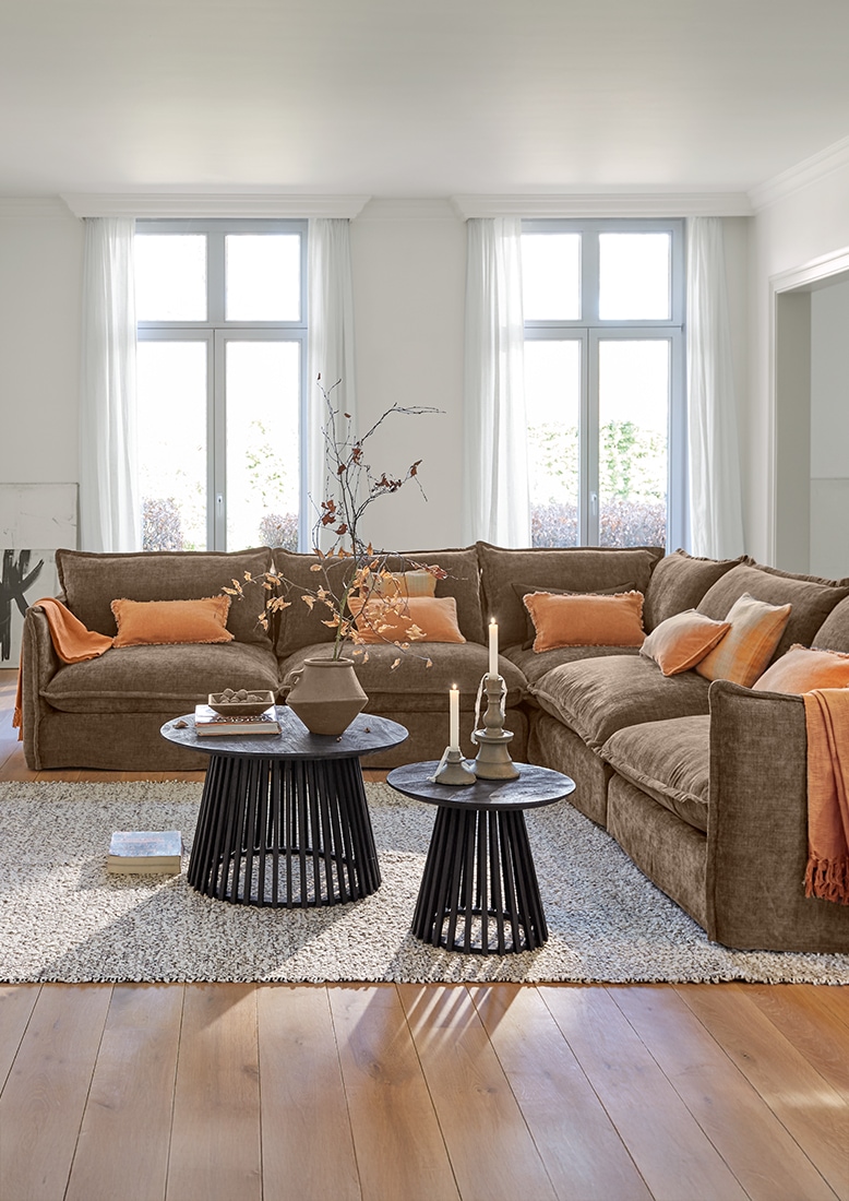 Gemütliches Wohnzimmer mit braunem Ecksofa und schwarzen Beistelltischen auf hellem Teppich