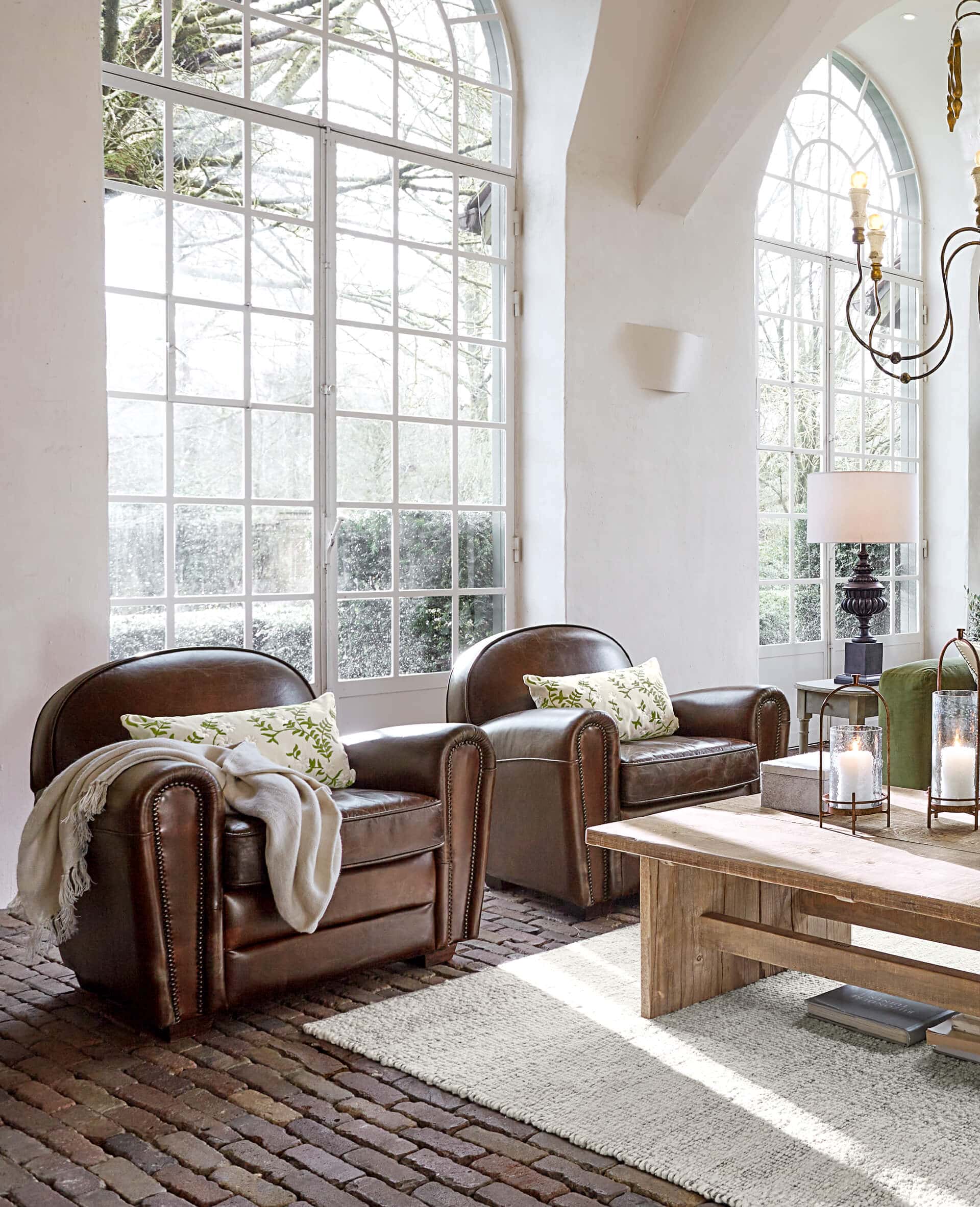 Zwei braune Ledersessel mit Kissen und Decke in hellem Wohnzimmer mit großen Fenstern