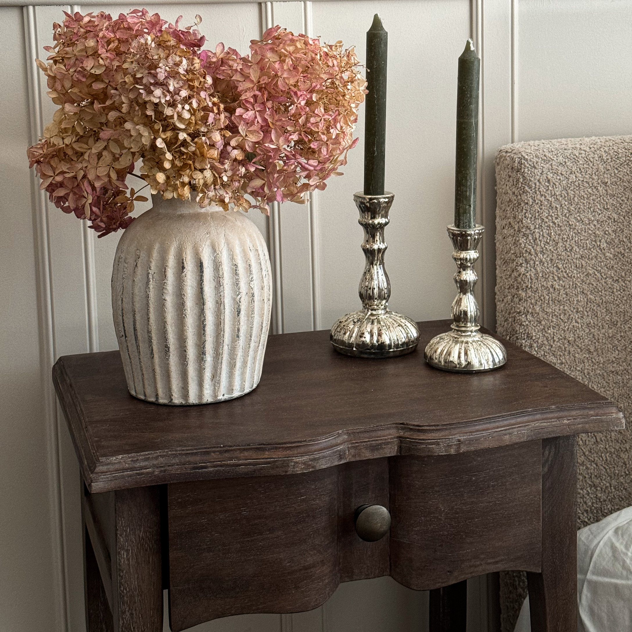 Beige Keramikvase mit getrockneten rosa Blüten auf dunklem Holztisch als Dekoration