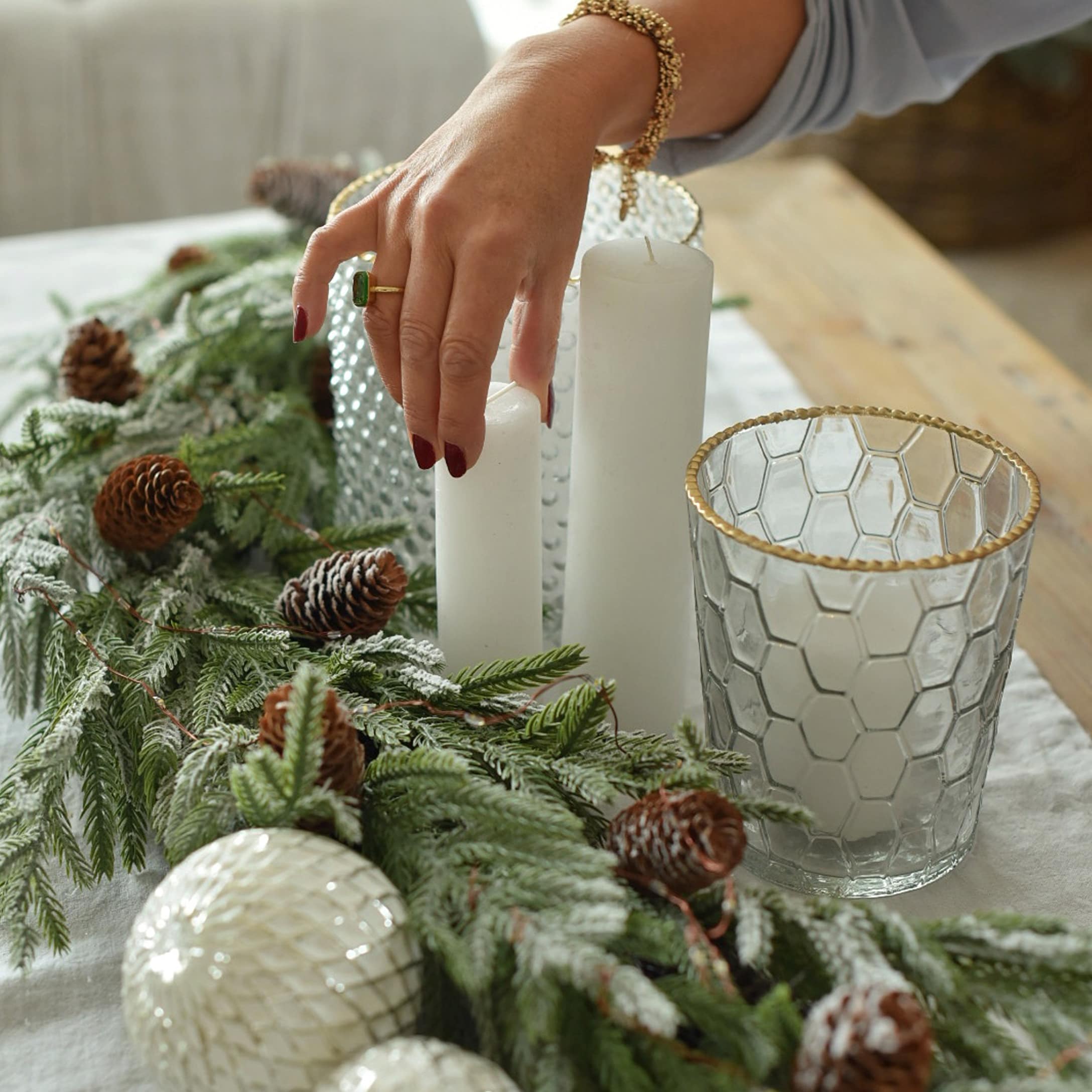 Weihnachtsdekoration mit weißen Kerzen, Glaswindlicht mit goldenem Rand und grünen Zweigen mit Zapfen