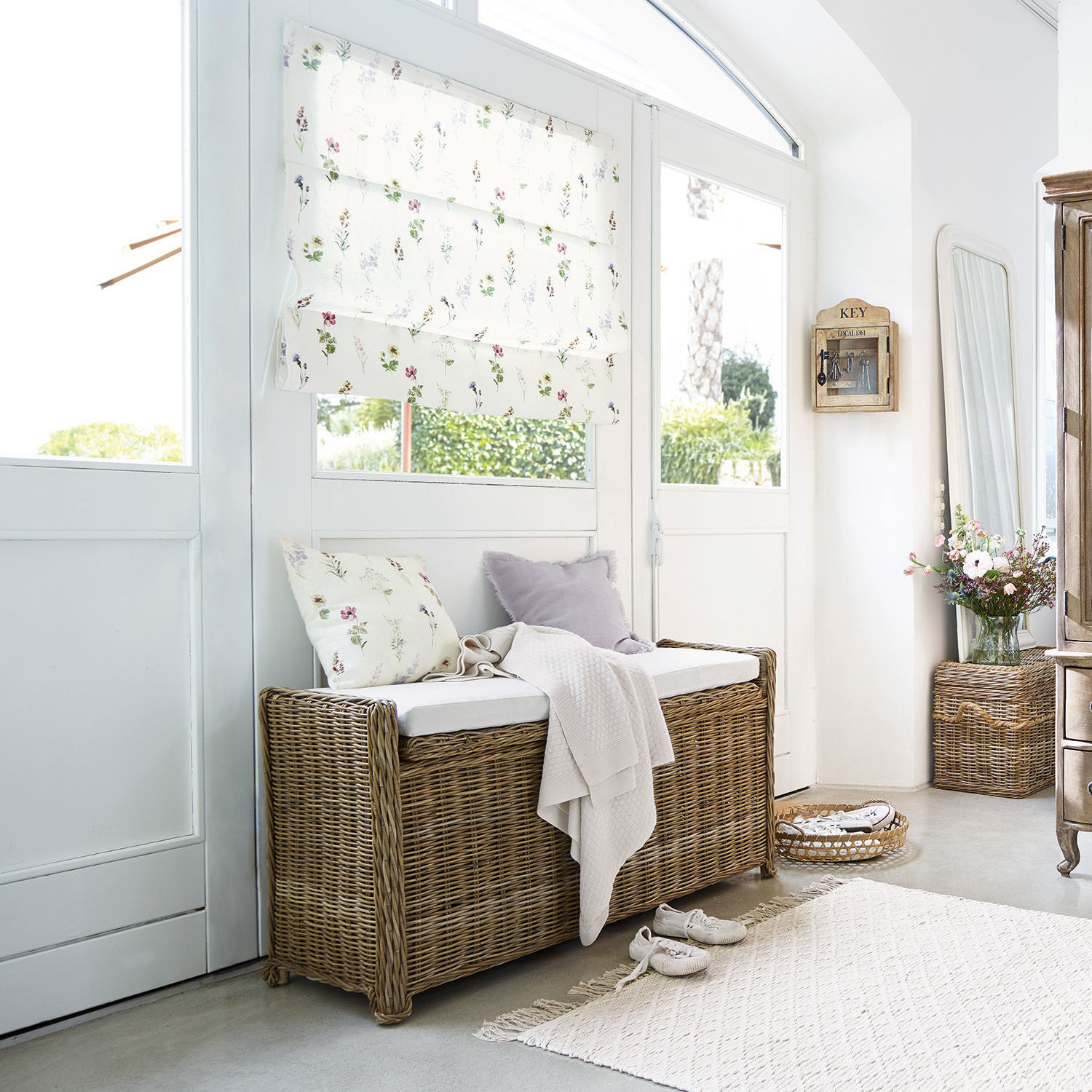 Rattanbank mit weißem Polster und floralen Kissen in hellem, gemütlichem Raum