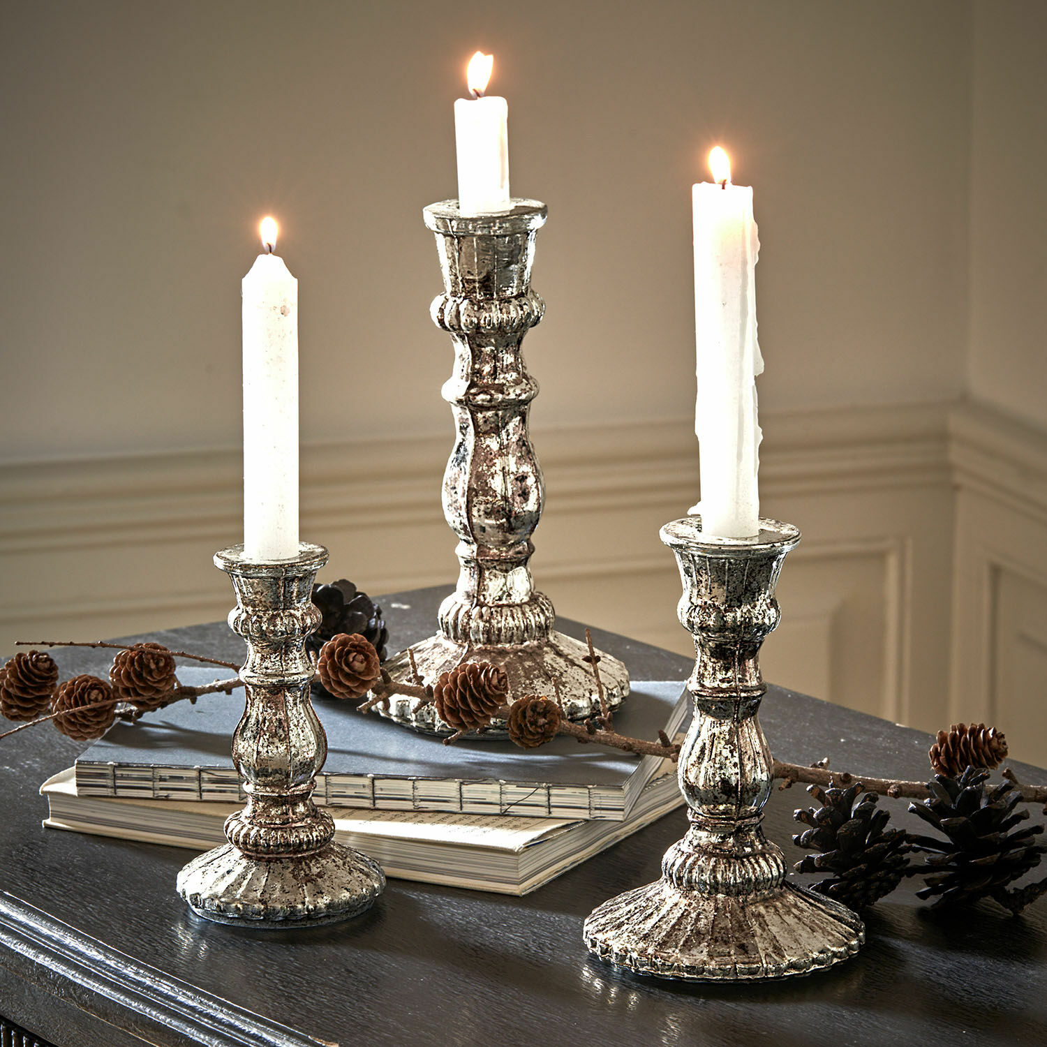 Kerzenständer 3er Set Favalina Drei vintage Metall-Kerzenhalter in Silber mit weißen Kerzen auf dunklem Tisch mit Kiefernzapfen dekoriert