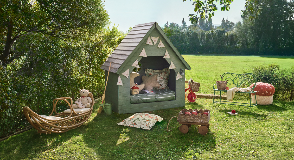 Grünes Holzspielhaus mit Kissen und Spielzeug auf der Wiese im Garten