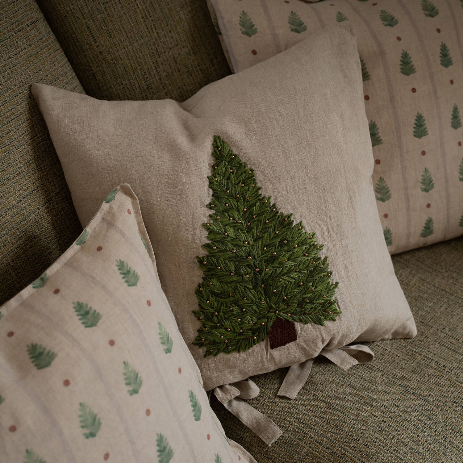 Beiges Leinenkissen mit grünem besticktem Tannenbaum und goldenen Perlen auf Sofa