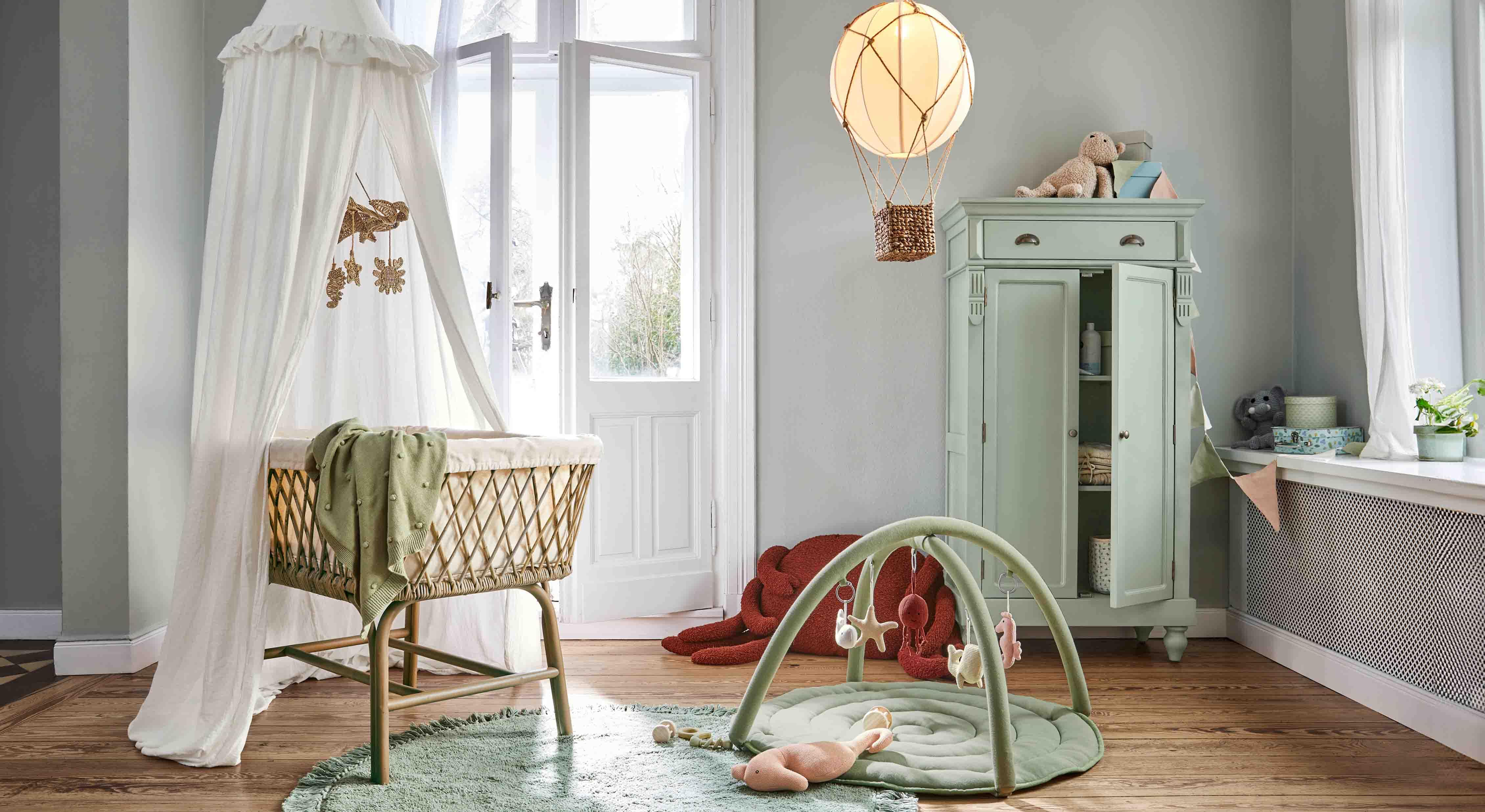 Gemütliches Kinderzimmer mit Korbwiege, grünem Teppich und pastellfarbenem Schrank für Spielzeug und Aufbewahrung