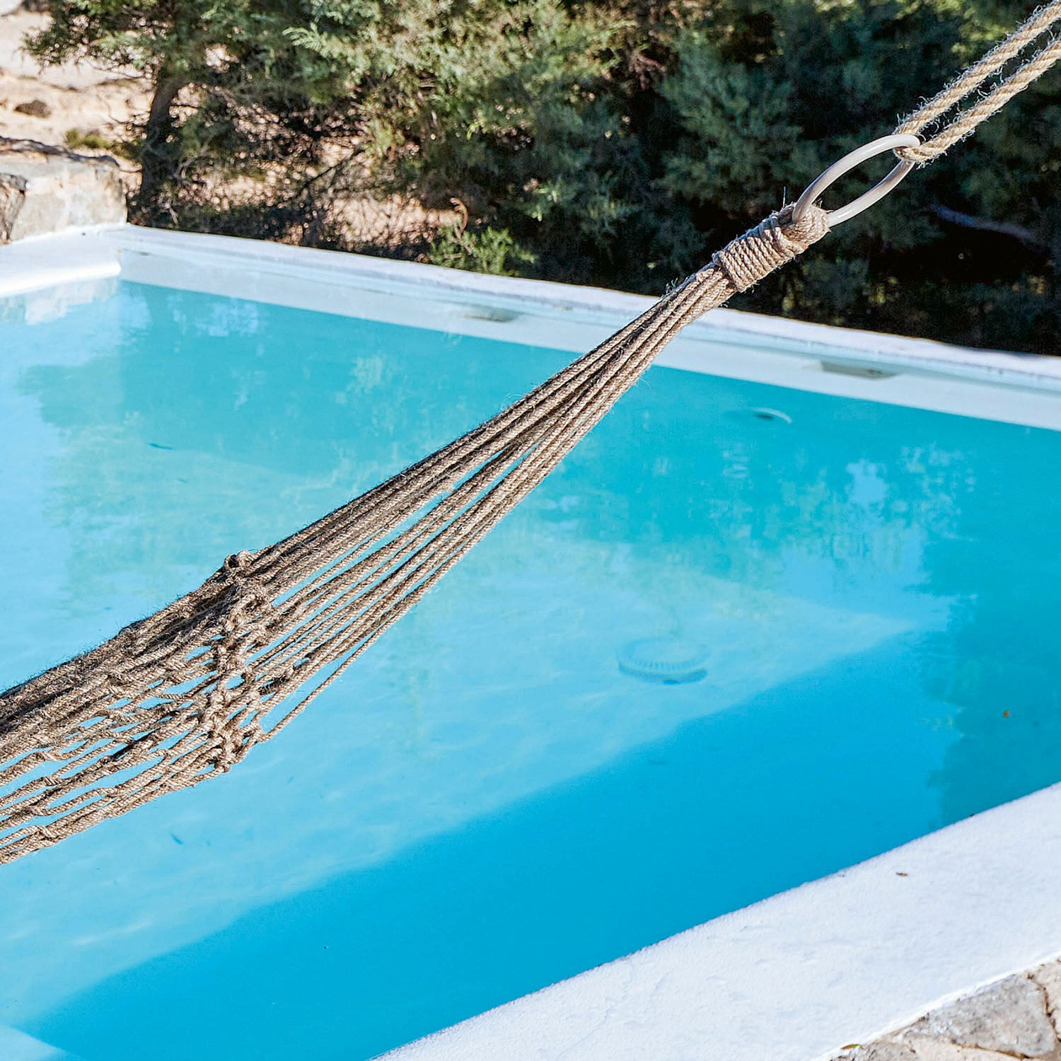 Beiger Naturfaser-Hängematte über blauem Pool, ideal zum Entspannen im Freien