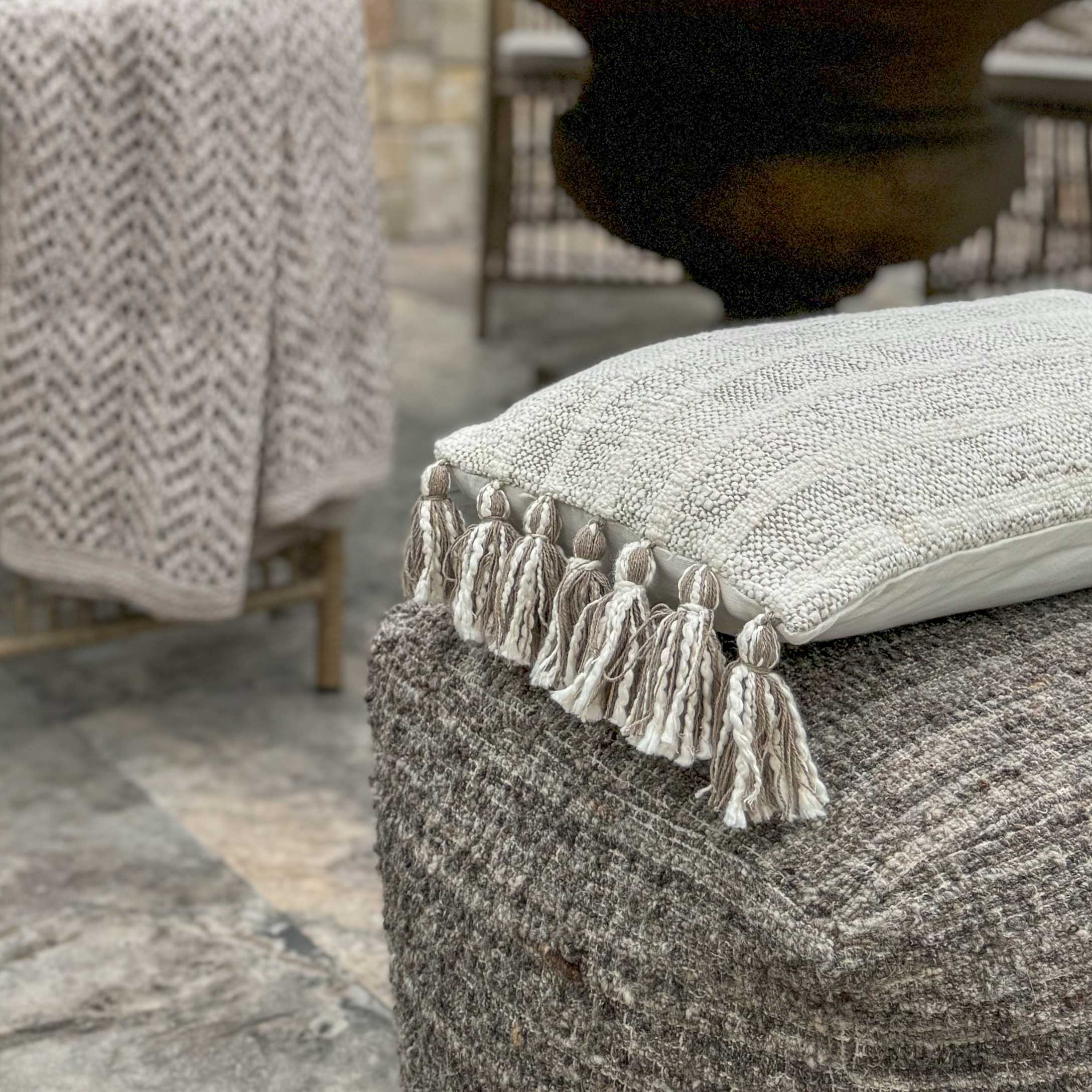 Beige Dekokissen mit Quasten auf grauem Wollhocker, gemütliche Wohntextilien