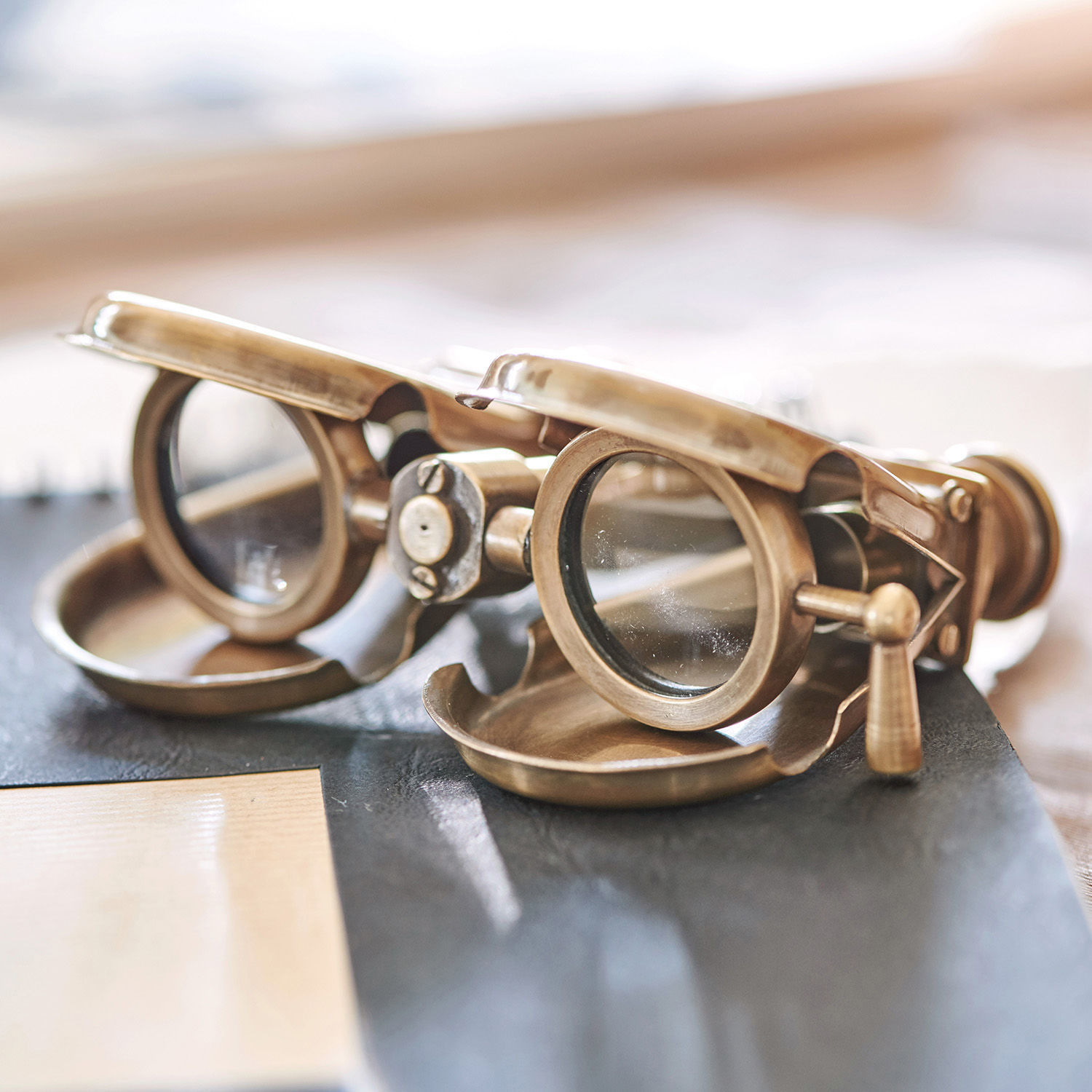 Antike Lesebrille aus Messing mit Schutzklappen auf den Gläsern auf einem Tisch
