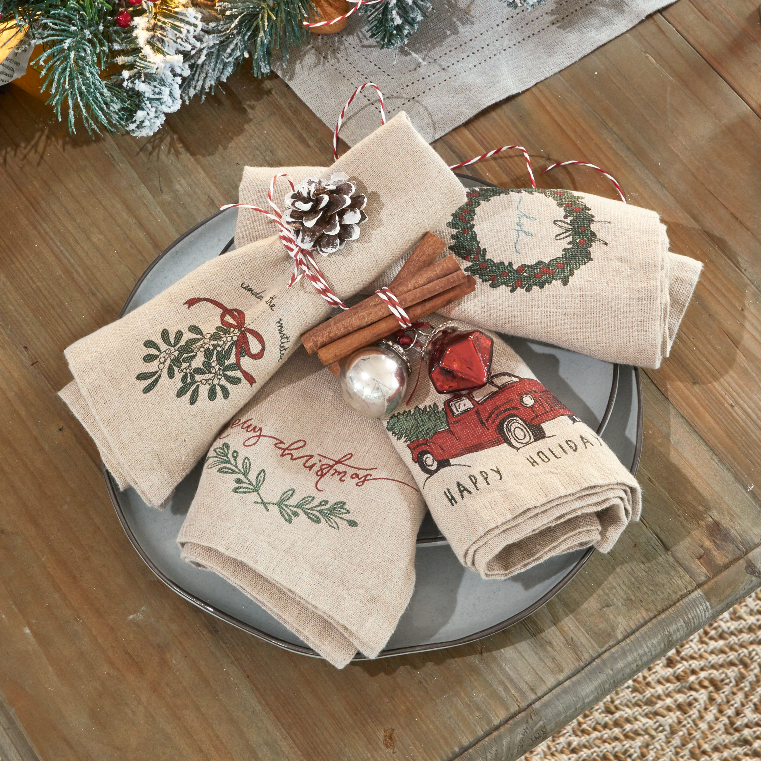 Leinen-Servietten mit Weihnachtsmotiven, dekoriert mit Zimtstangen und Tannenzapfen auf grauem Teller