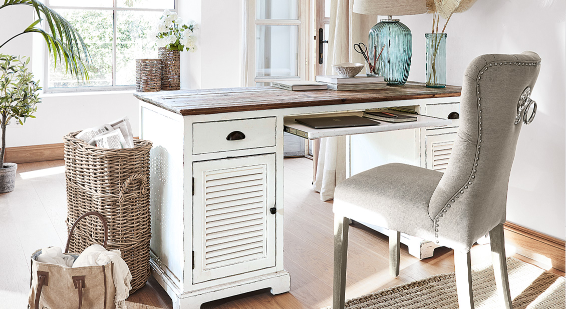 Weißes Holzschreibtisch im Shabby-Chic-Stil mit Schubladen und grauem Polsterstuhl in hellem Raum