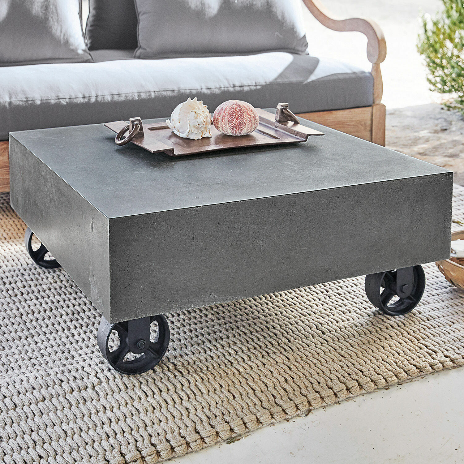 Quadratischer Couchtisch aus grauem Beton auf schwarzen Rollen auf hellem Teppich
