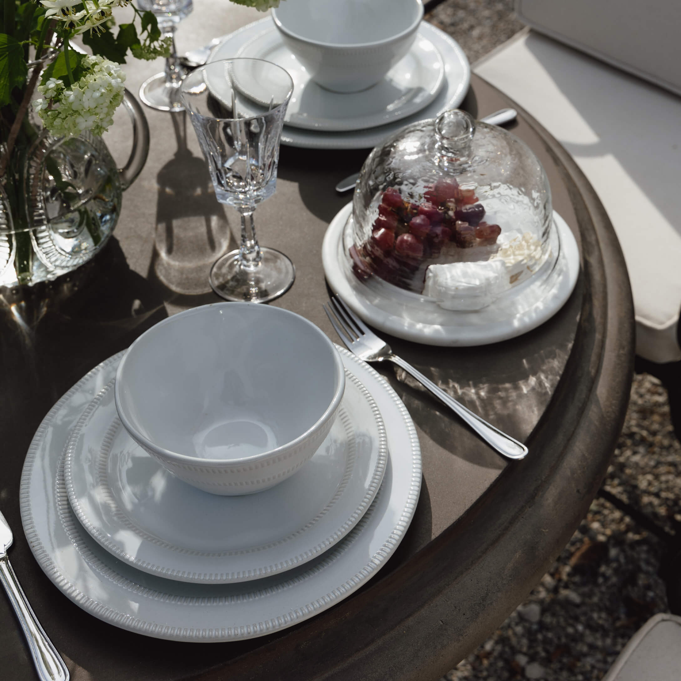 Weißes Porzellanservice auf braunem Tisch mit Glas und Glashaube für Trauben und Käse