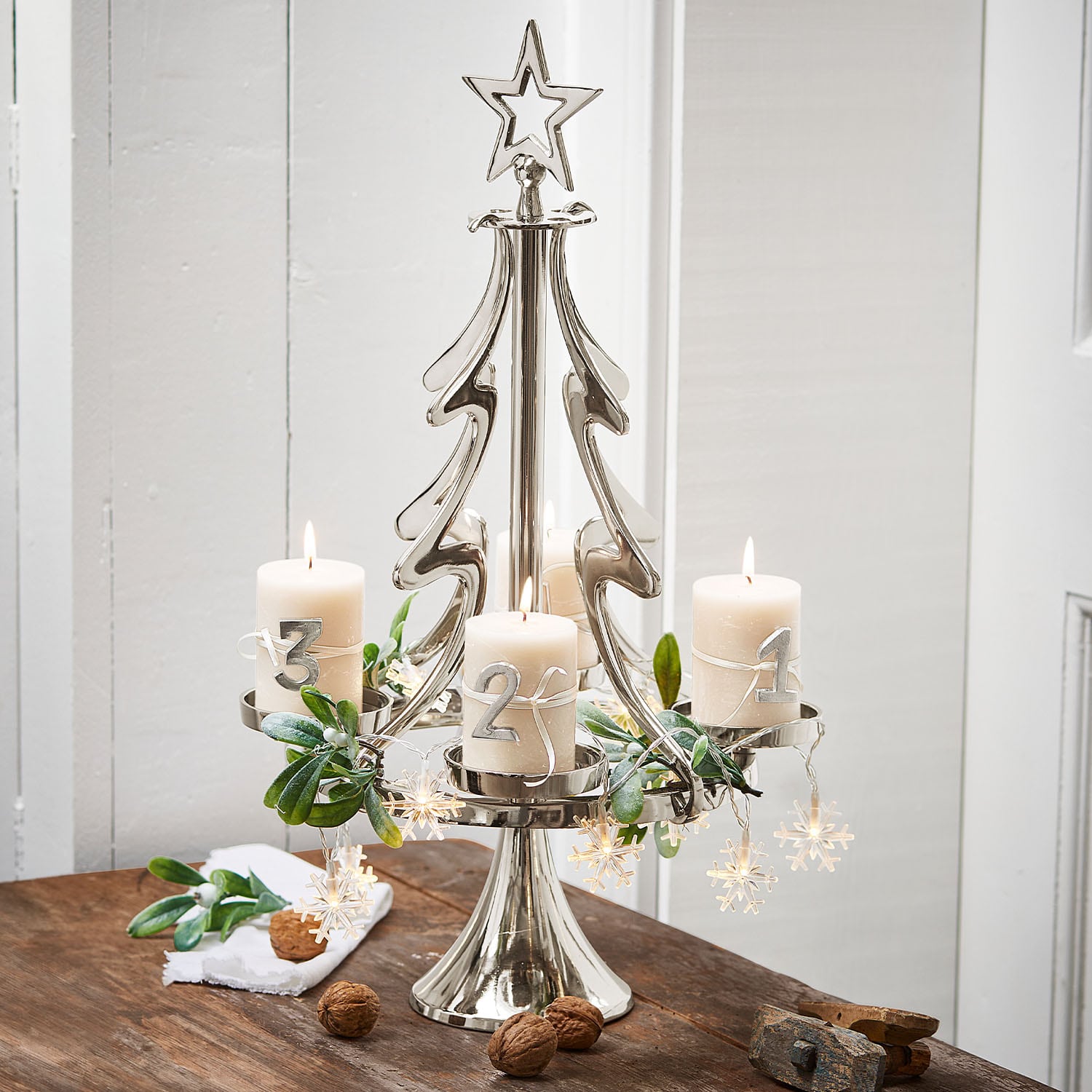 Metall-Adventskranz in Tannenbaumform mit vier weißen Kerzen und Weihnachtsdeko auf Holztisch