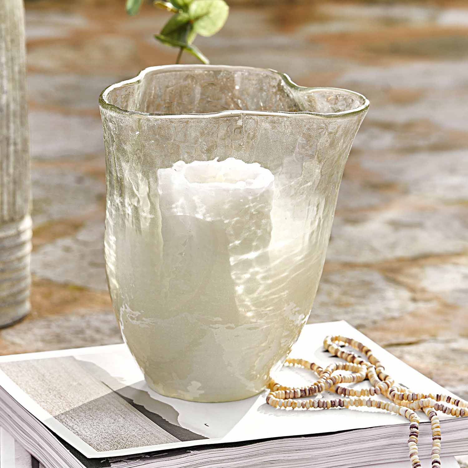 Transparenter Glaswindlicht mit weißer Kerze auf offenem Buch, stilvolle Tischdekoration