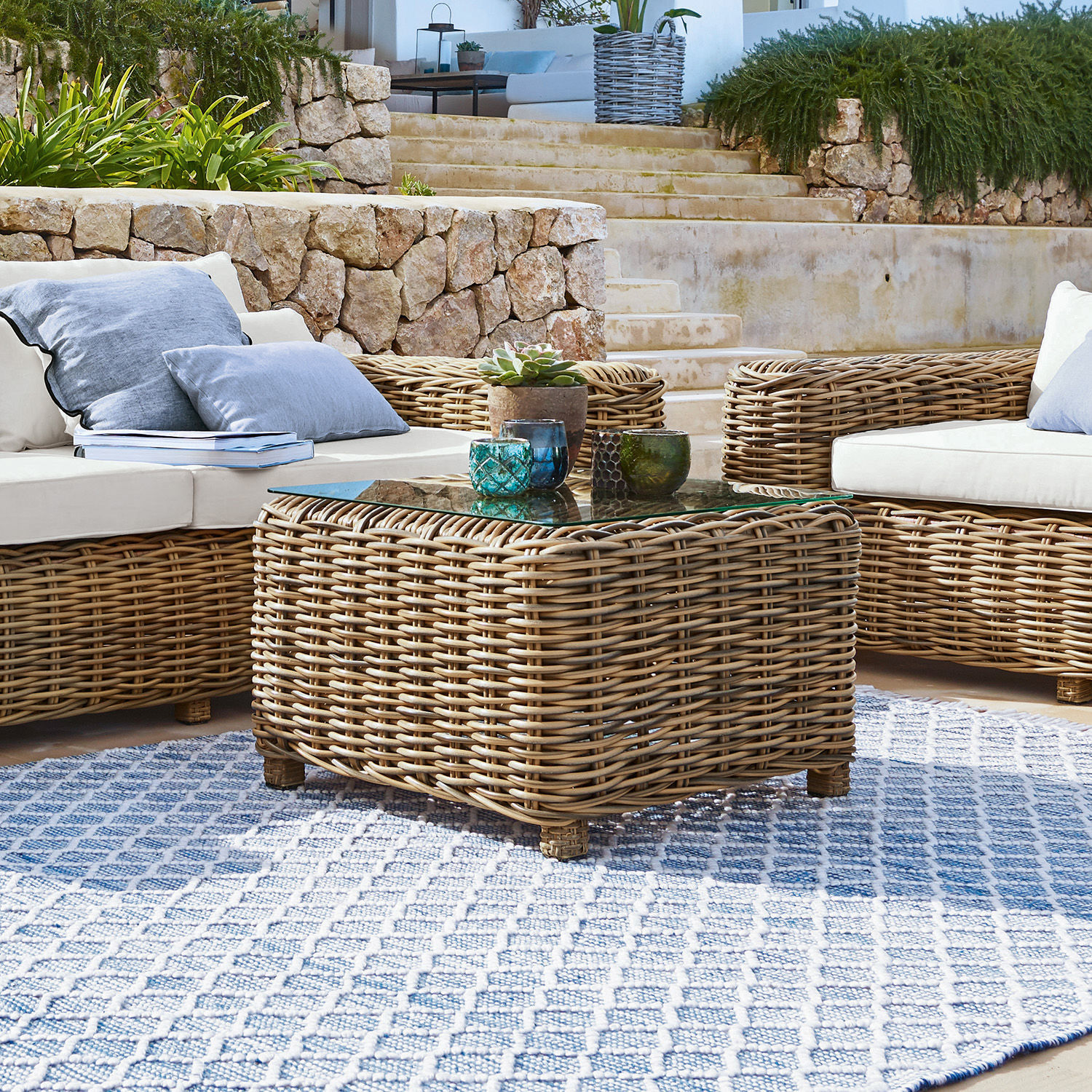 Gartenmöbel-Set aus natürlichem Rattan mit weißen Kissen und blauem Teppich im Außenbereich