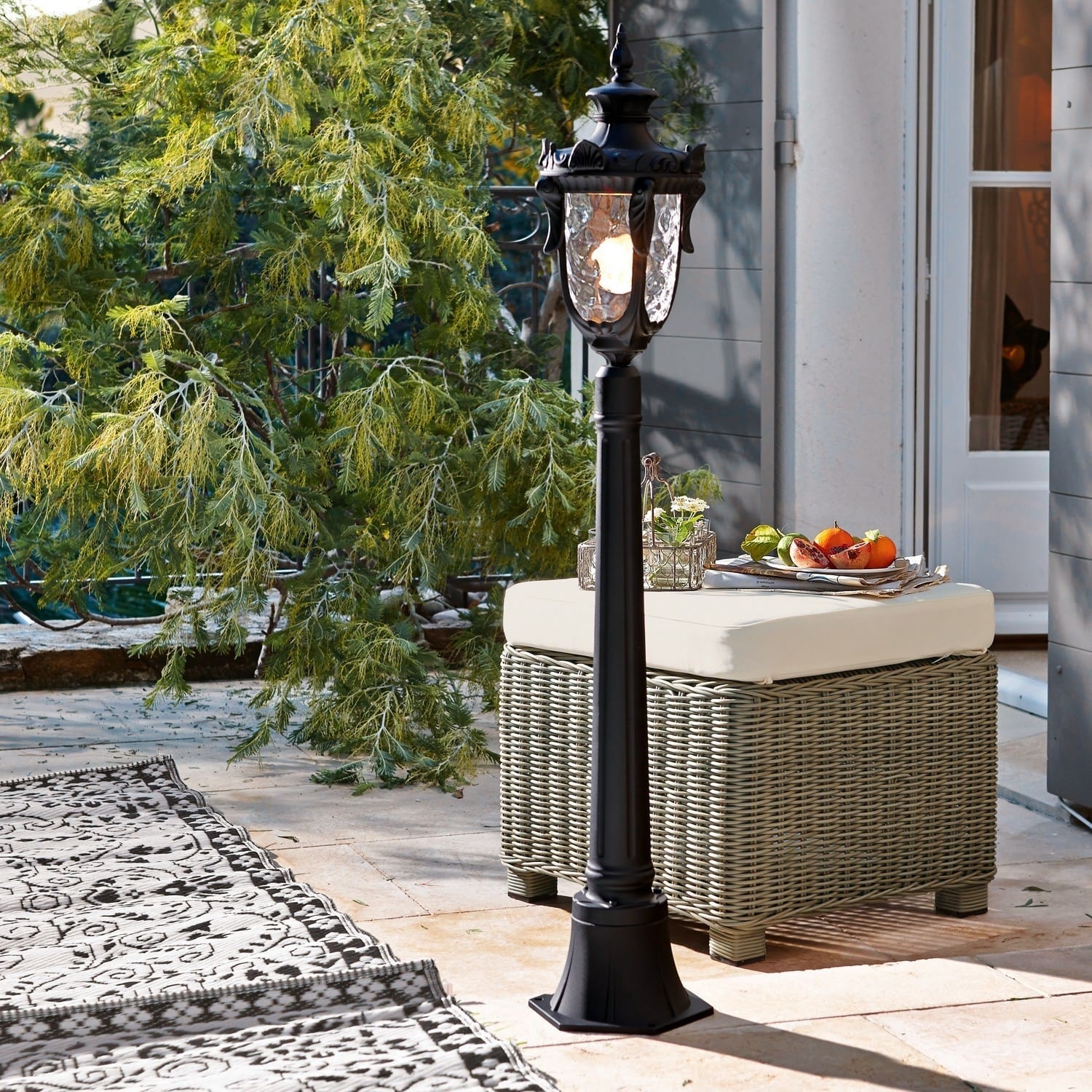 Schwarze Metall-Gartenlaterne mit dekorativem Glas auf Terrasse mit Rattanmöbeln