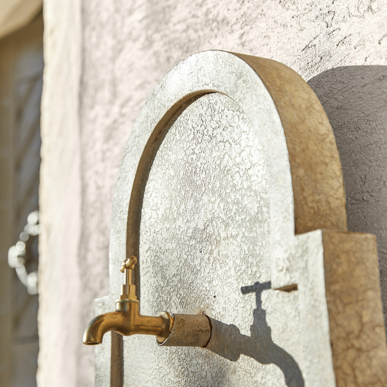 Goldener Messing-Wasserhahn an hellgrauer strukturierter Wand mit Schatten, Gartendekor