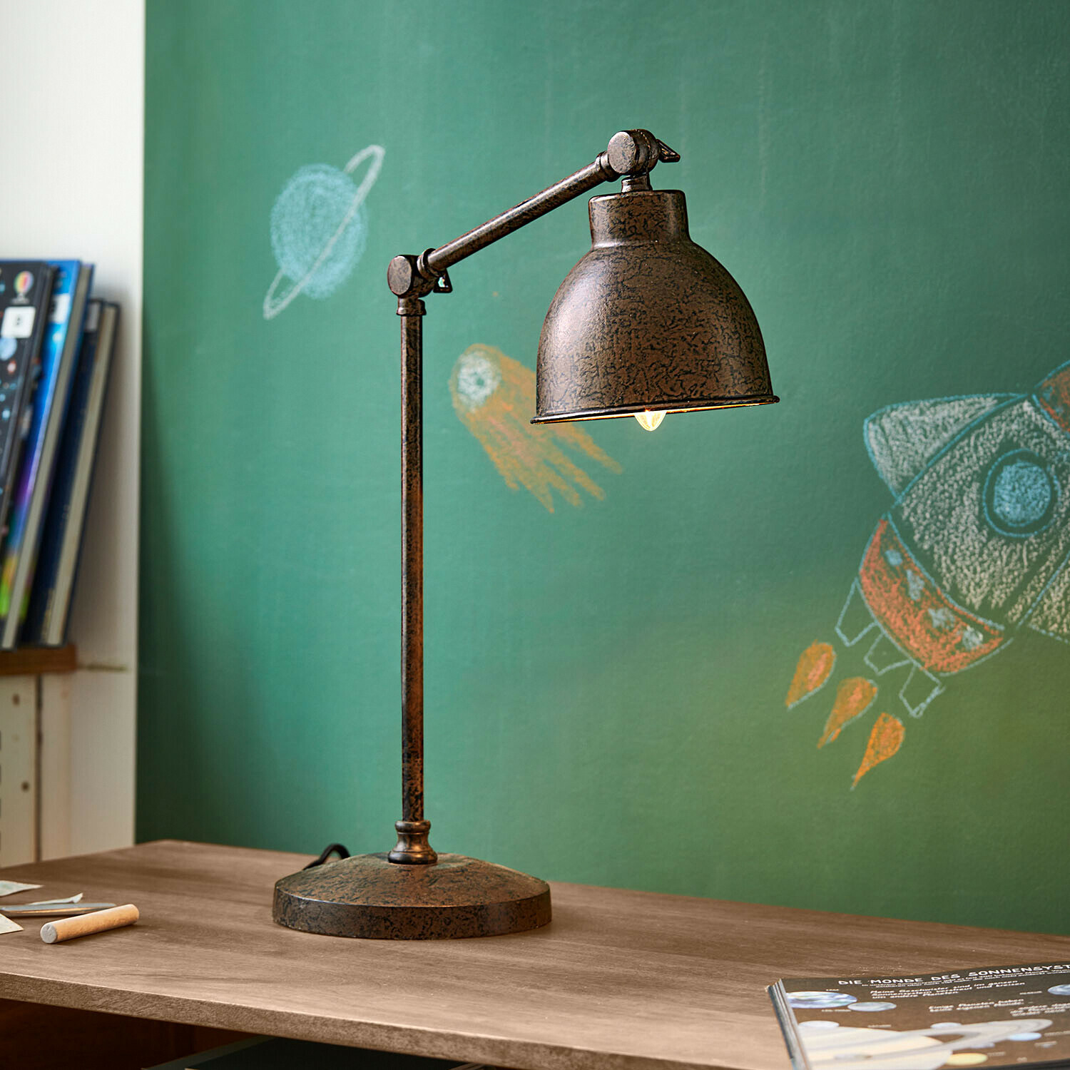 Vintage Metall-Schreibtischlampe in rostbraun auf Holztisch vor grüner Tafel mit Weltraummotiven