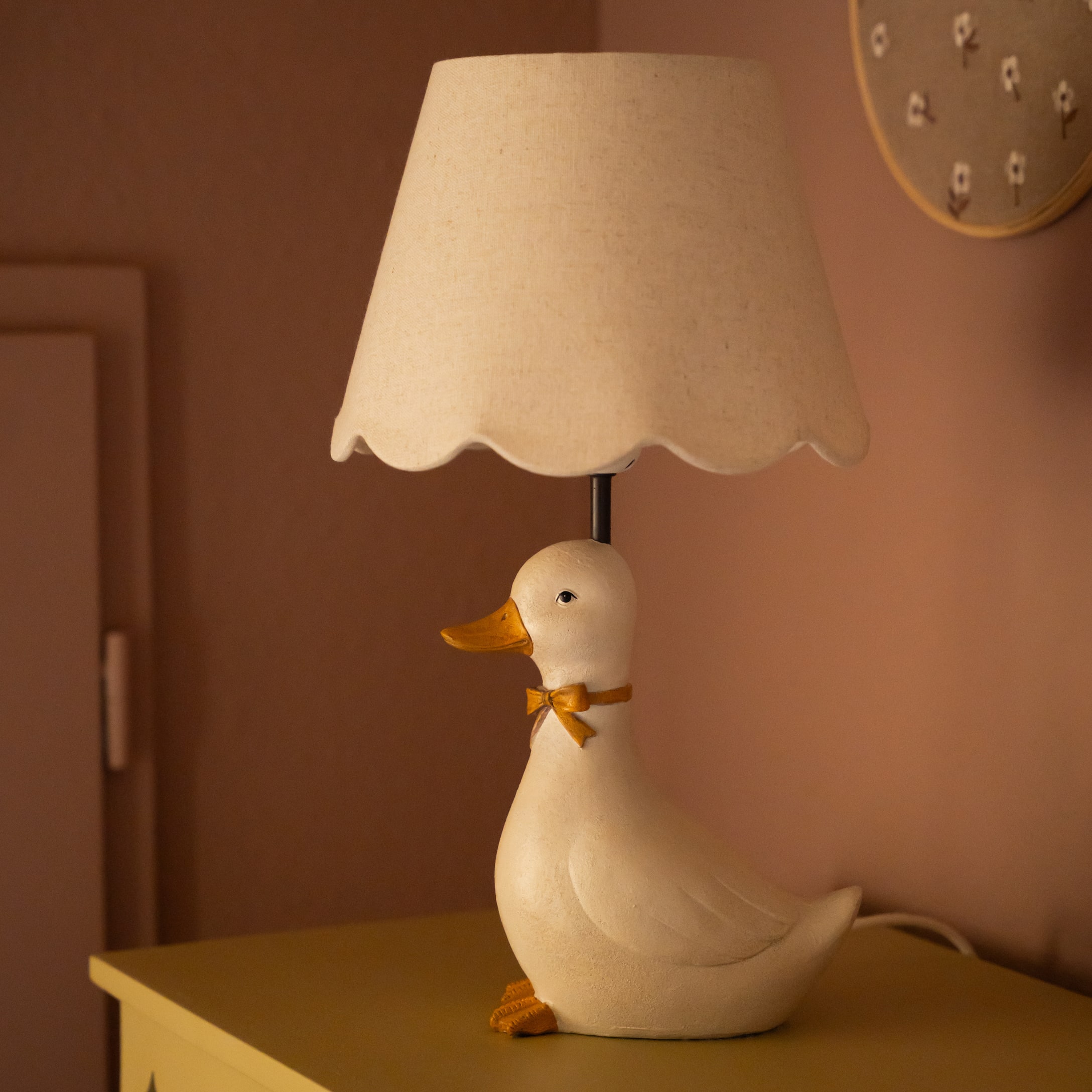 Tischlampe in Entenform aus weißem Material mit beigem Lampenschirm und oranger Schleife
