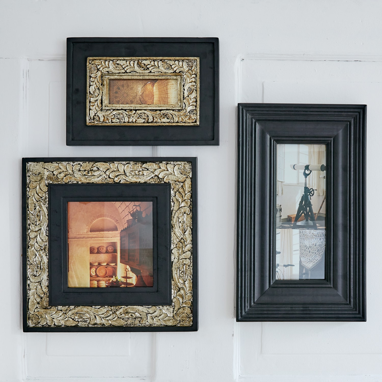 Drei schwarze Bilderrahmen mit goldenen Verzierungen und Vintage-Fotos an weißer Wand