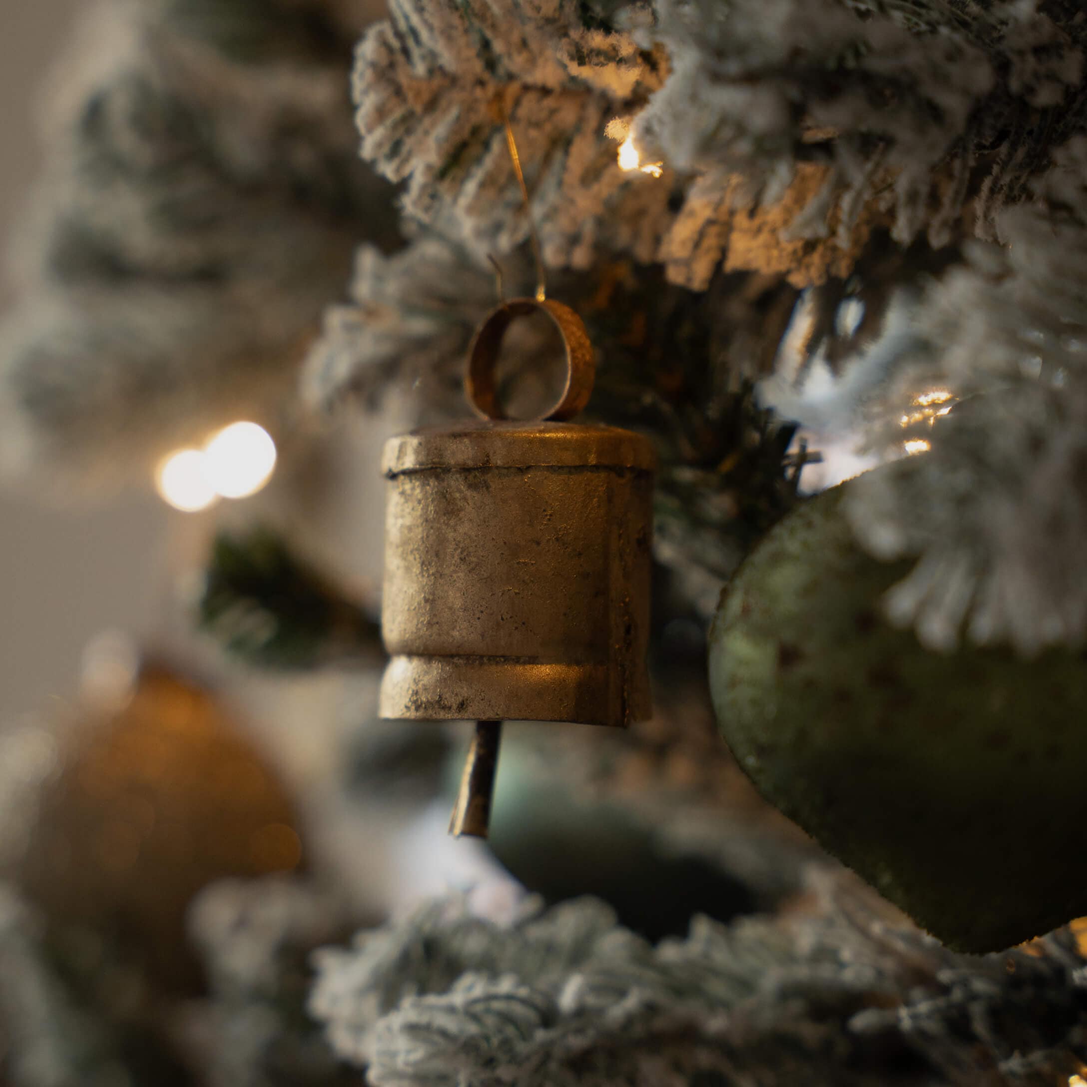 Goldener Metallglöckchen-Anhänger an schneebedecktem Weihnachtsbaum mit festlicher Dekoration