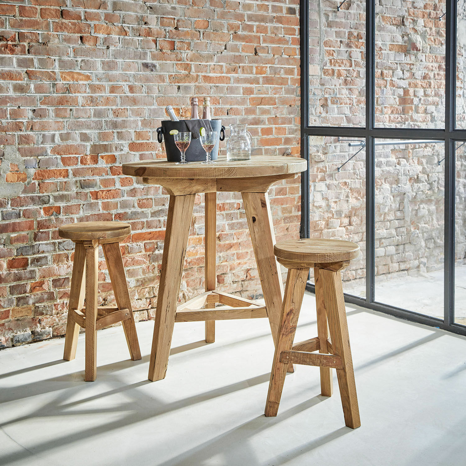 Heller Holzbartisch mit zwei passenden Hockern vor Ziegelwand und großen Fenstern im Industrie-Stil