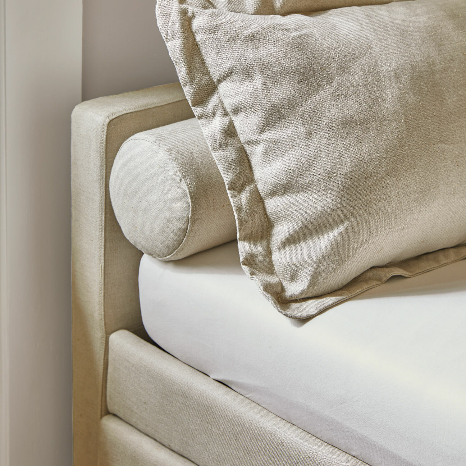 Beige Leinenkissen und Nackenrolle auf hellem Bett, natürliche Schlafzimmertextilien
