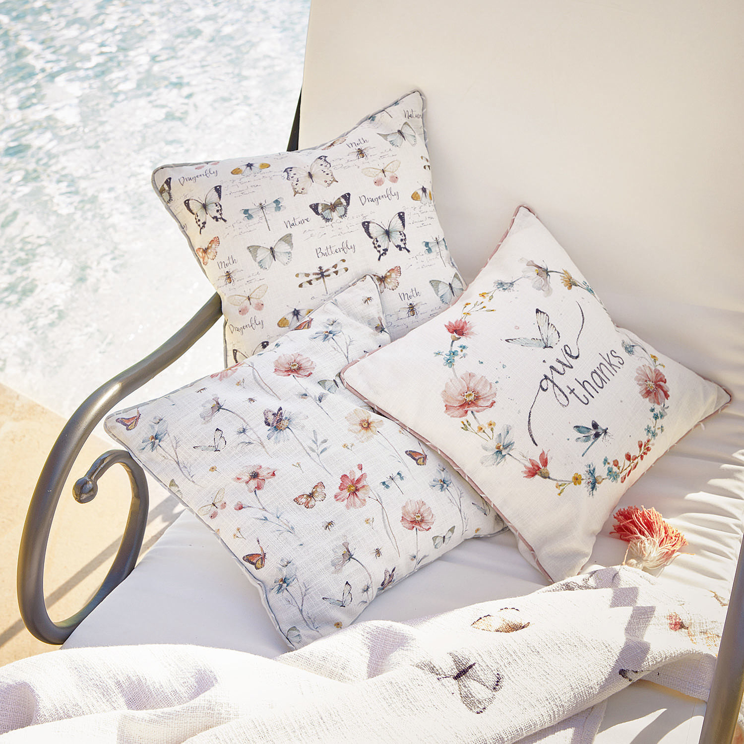 Drei helle Kissen mit Schmetterlings- und Blumenmuster auf weißem Stoff, Wohnaccessoire