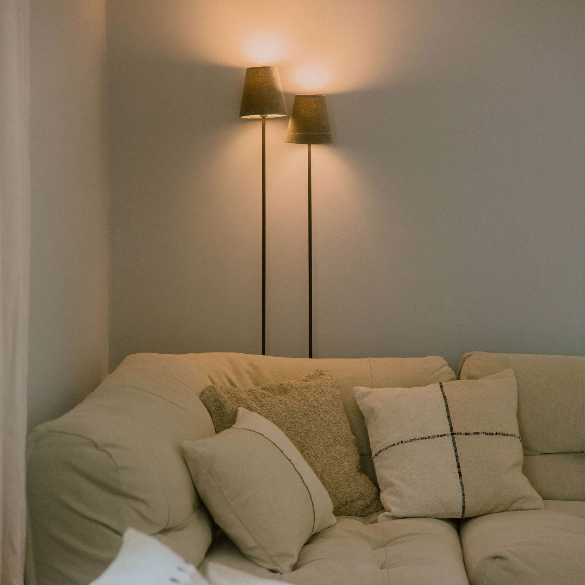 Beige Sofa mit weichen Kissen und zwei Stehlampen mit dunklen Lampenschirmen im Wohnzimmer