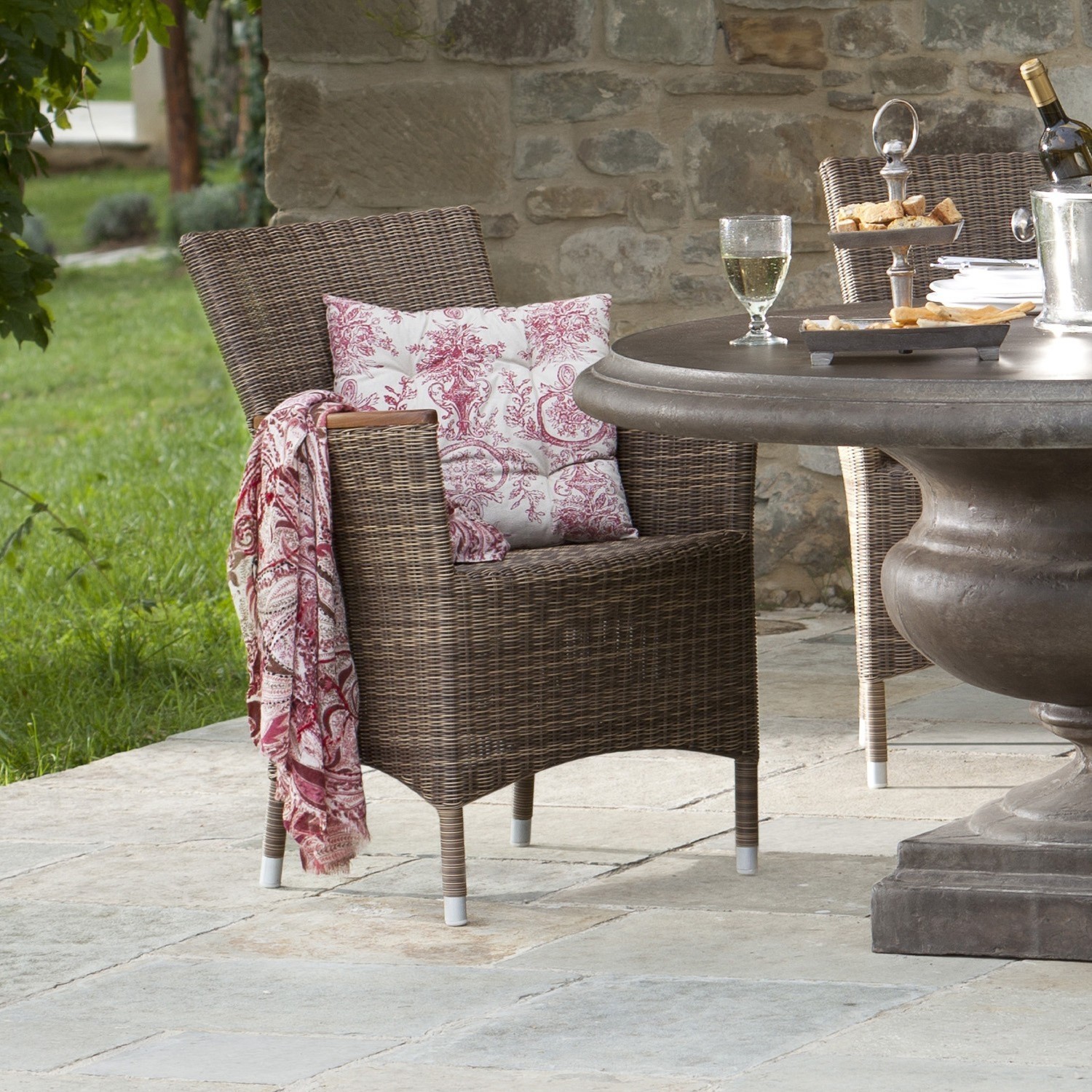 Brauner Rattanstuhl auf Terrasse mit Kissen und rot gemustertem Plaid, Gartenmöbel