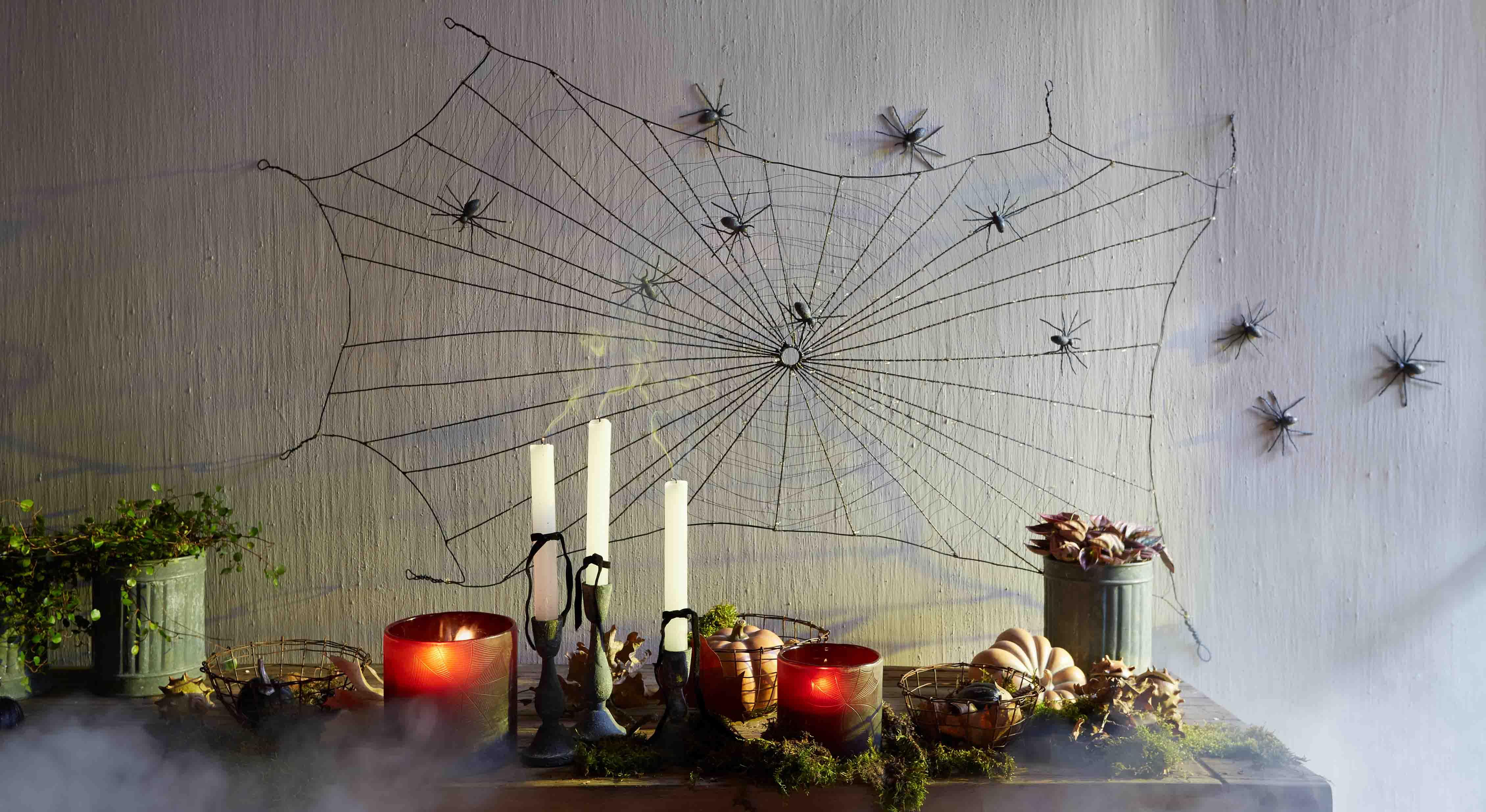 Halloween-Dekoration mit schwarzem Spinnennetz und Plastikspinnen an der Wand, Kerzen und Kürbisse auf dem Tisch