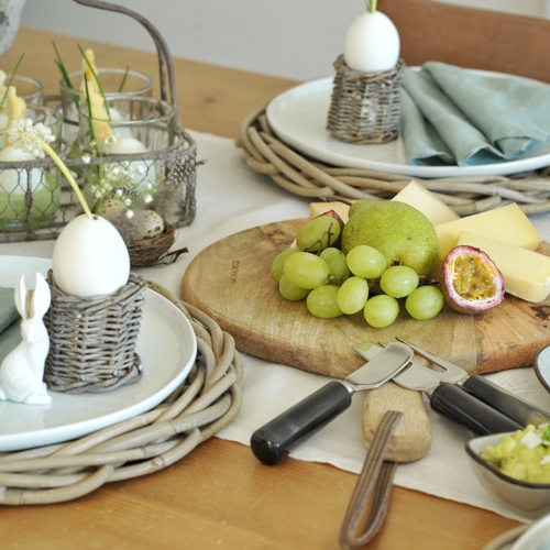 Osterbrunch-Tisch mit Holzbrett, Trauben, Birne, Käse und Eierdekorationen aus Weide