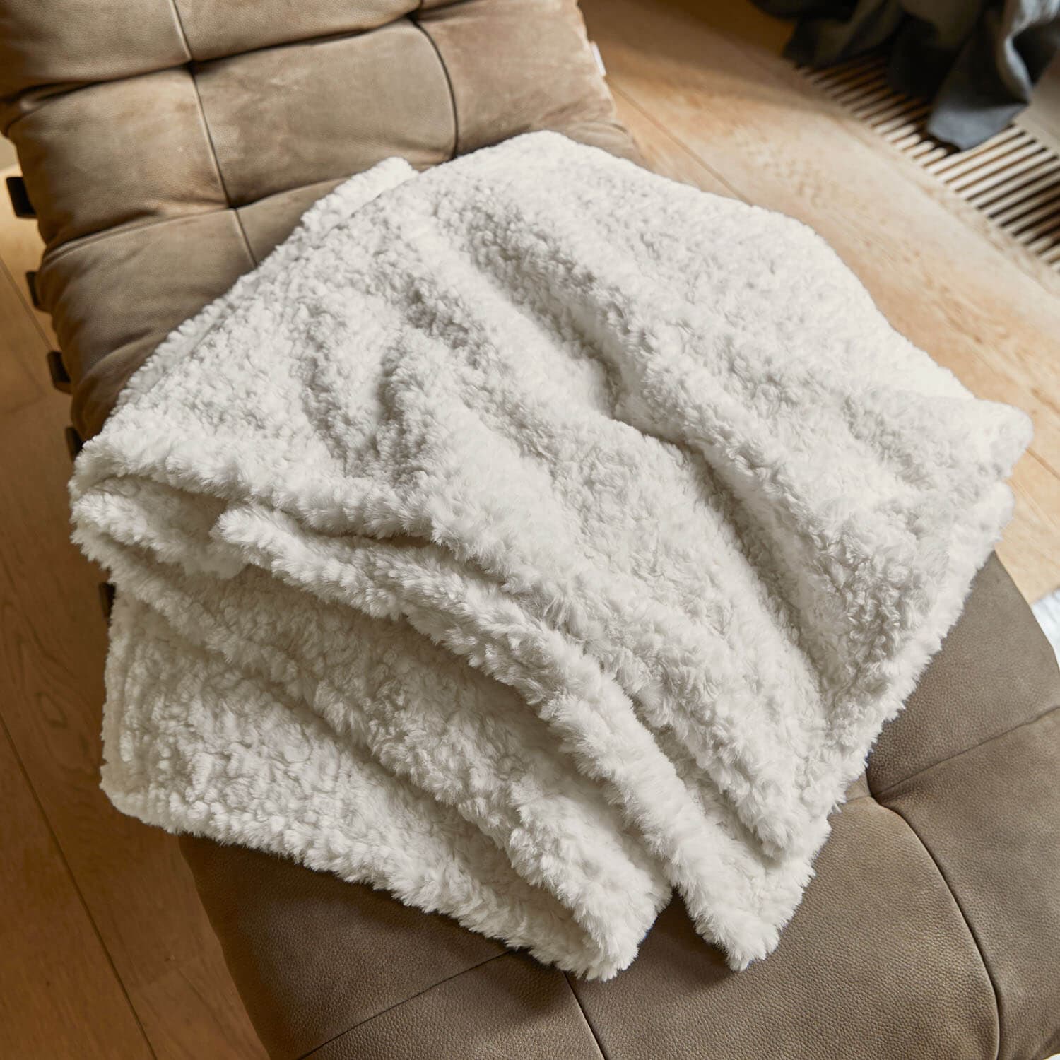 Weiche weiße Kuscheldecke aus Plüschmaterial auf braunem Sessel, ideal für Wohnzimmer