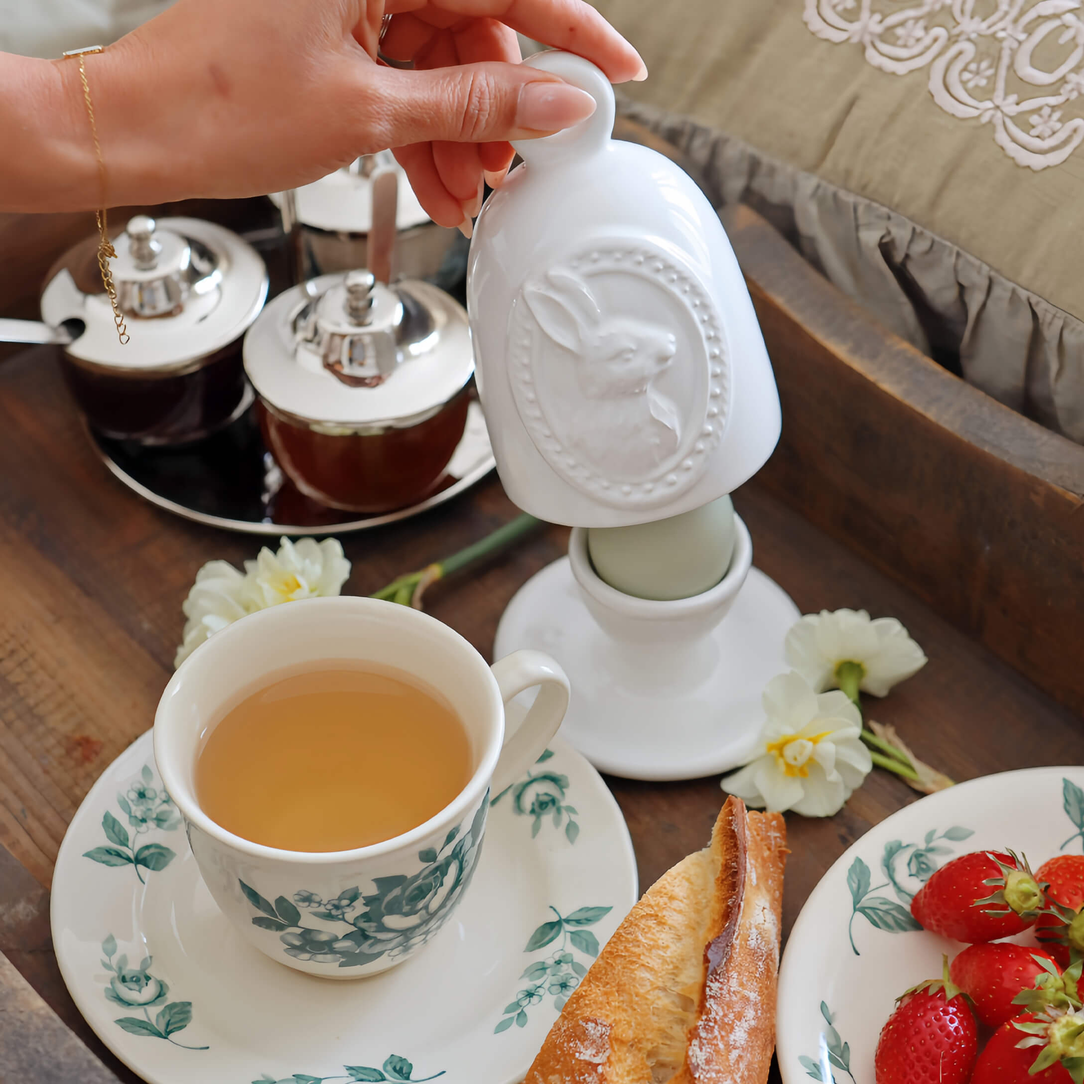 Weißer Keramikbehälter mit Hasenmotiv auf Frühstückstisch mit Tee und Erdbeeren