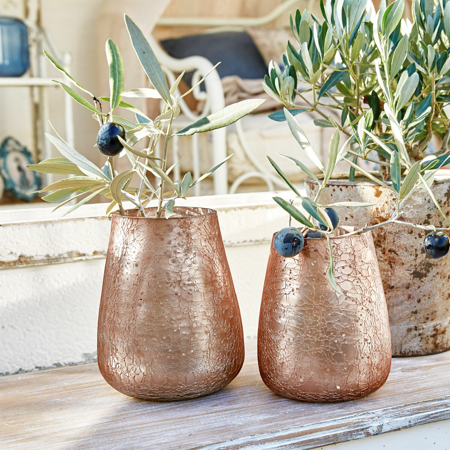 Zwei kupferfarbene Glasvasen mit rissiger Struktur und Olivenzweigen auf Holztisch