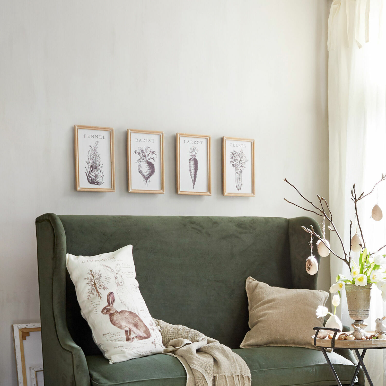 Grünes Samtsofa mit dekorativen Kissen und Gemüsebildern an der Wand in hellem Wohnzimmer