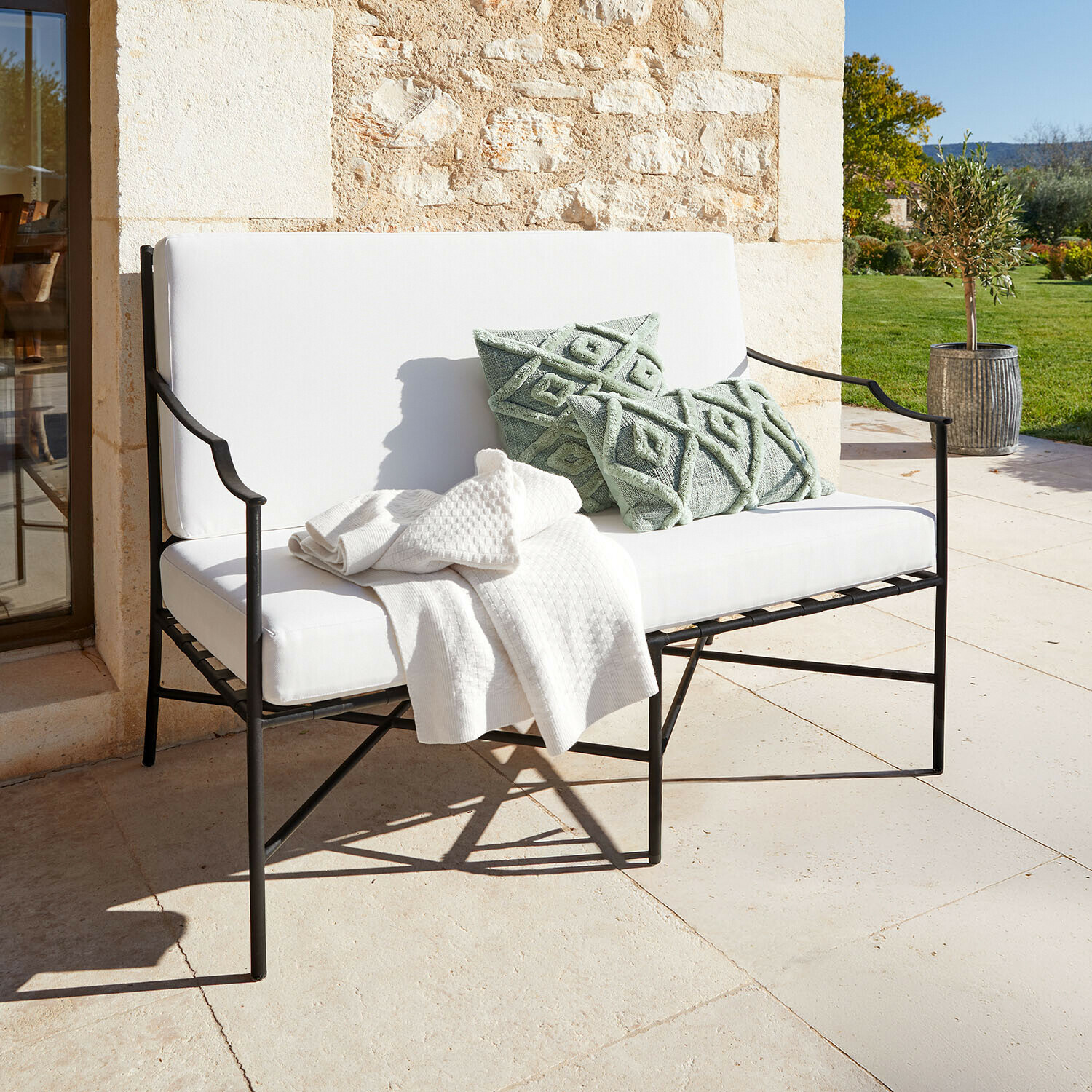Sofa Vexford Weiße Metall-Gartenbank mit weichen Polstern und grünen Dekokissen auf sonniger Terrasse