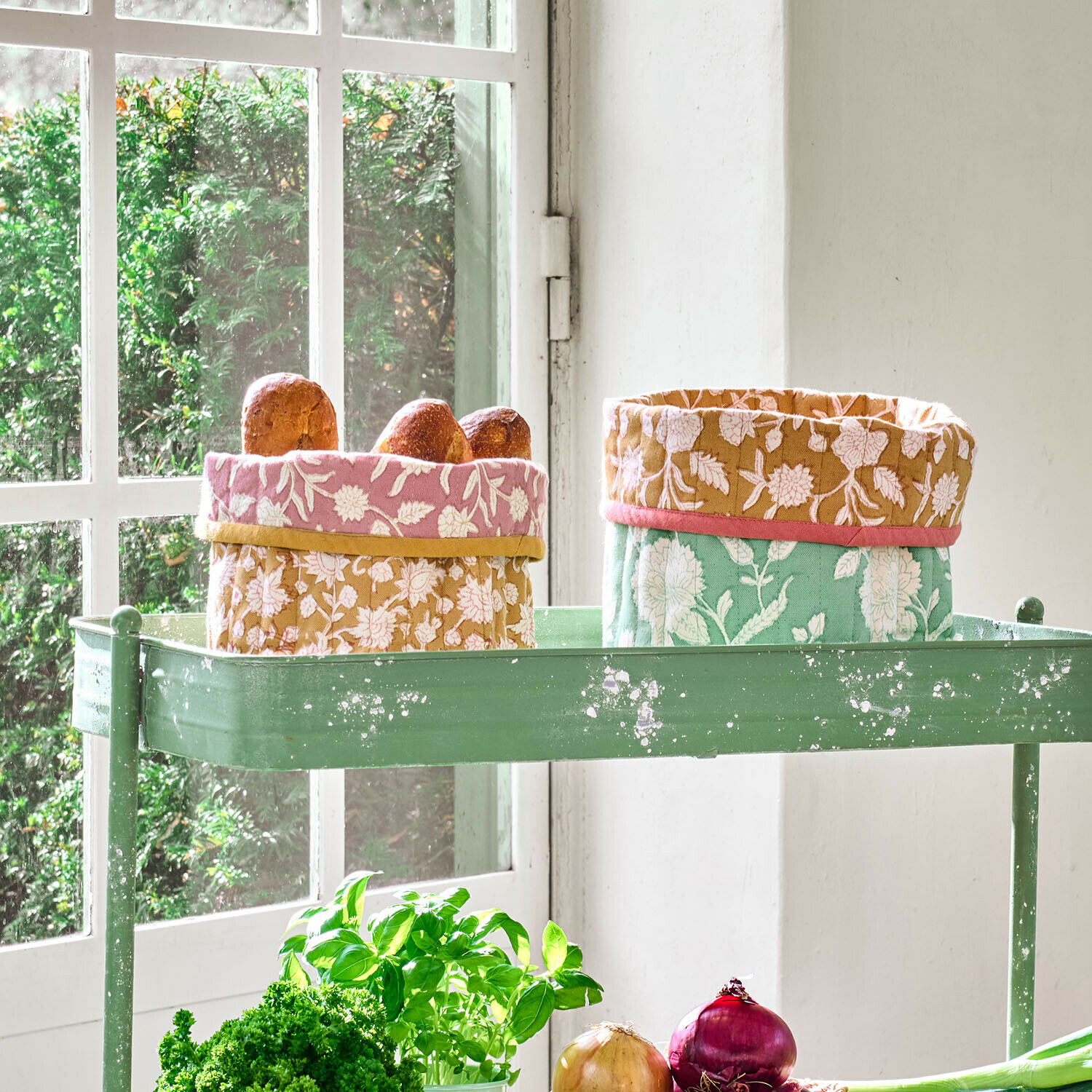 Zwei bunte Baumwollkörbe mit Blumenmuster auf grünem Metalltisch mit Brot und Kräutern