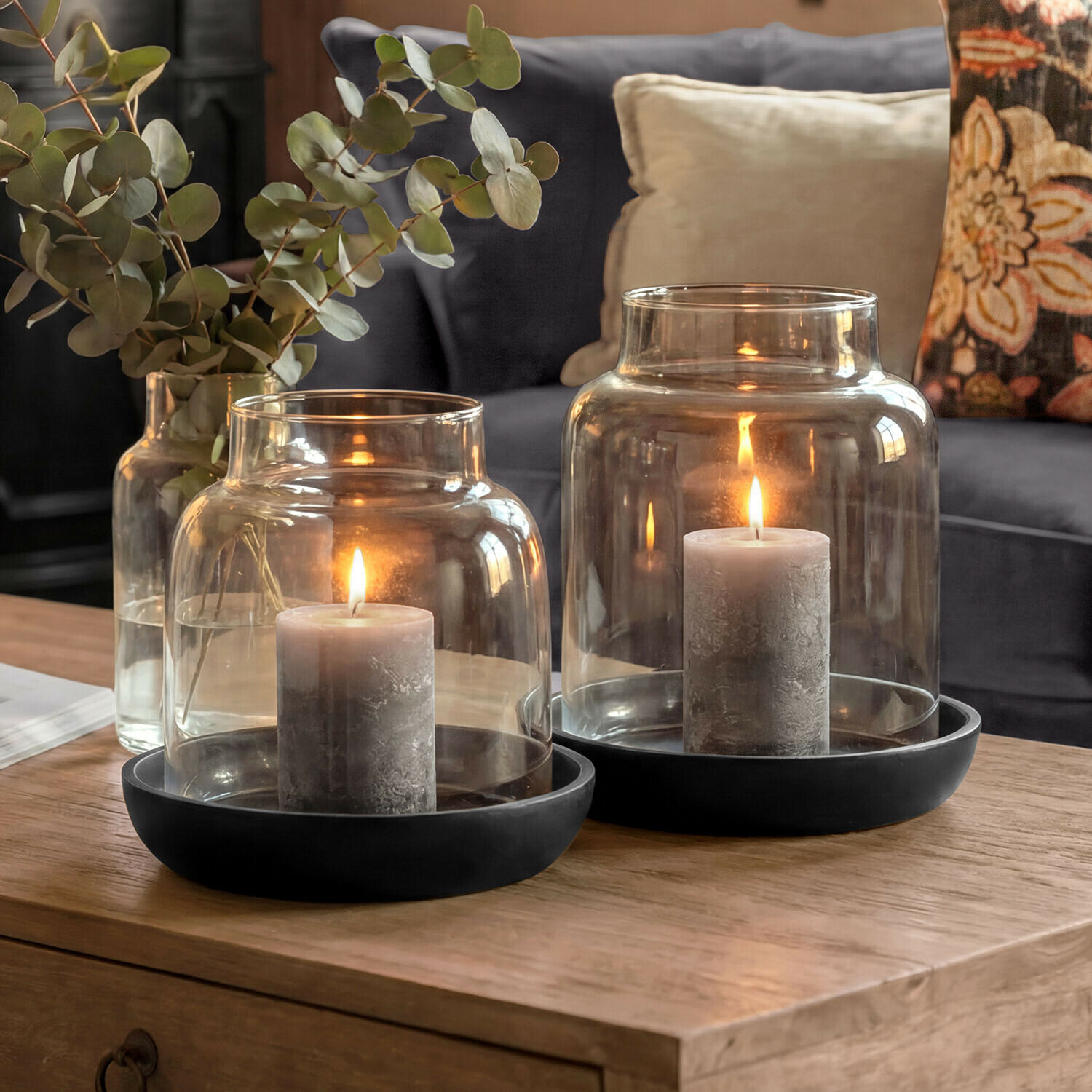 Windlicht 2er Set Venturio Graue Kerzen in Glaslaternen mit schwarzen Sockeln auf Holztisch im Wohnzimmer