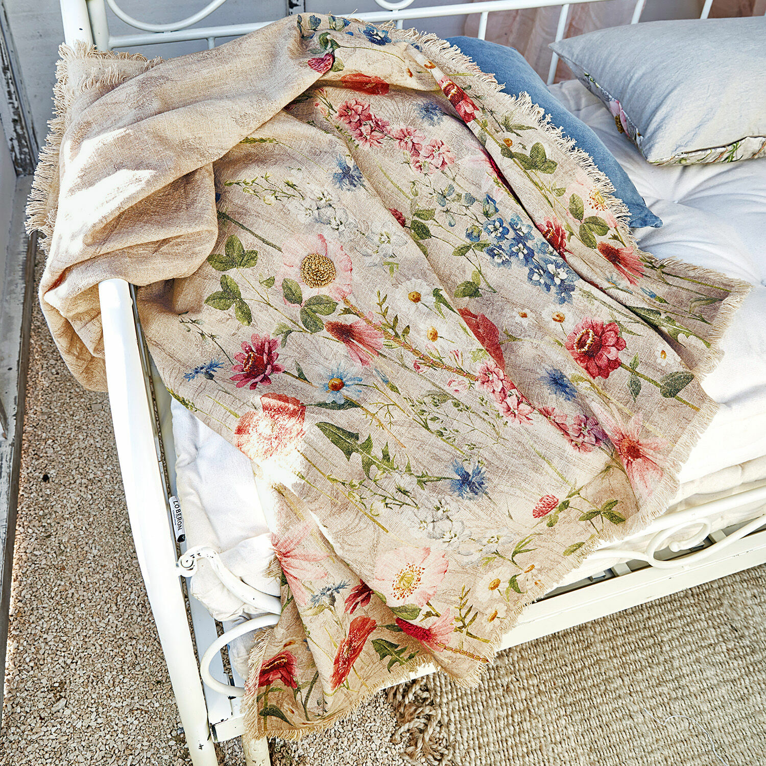 Beige Leinen-Decke mit buntem Blumenmuster und Fransen auf weißem Metallbett