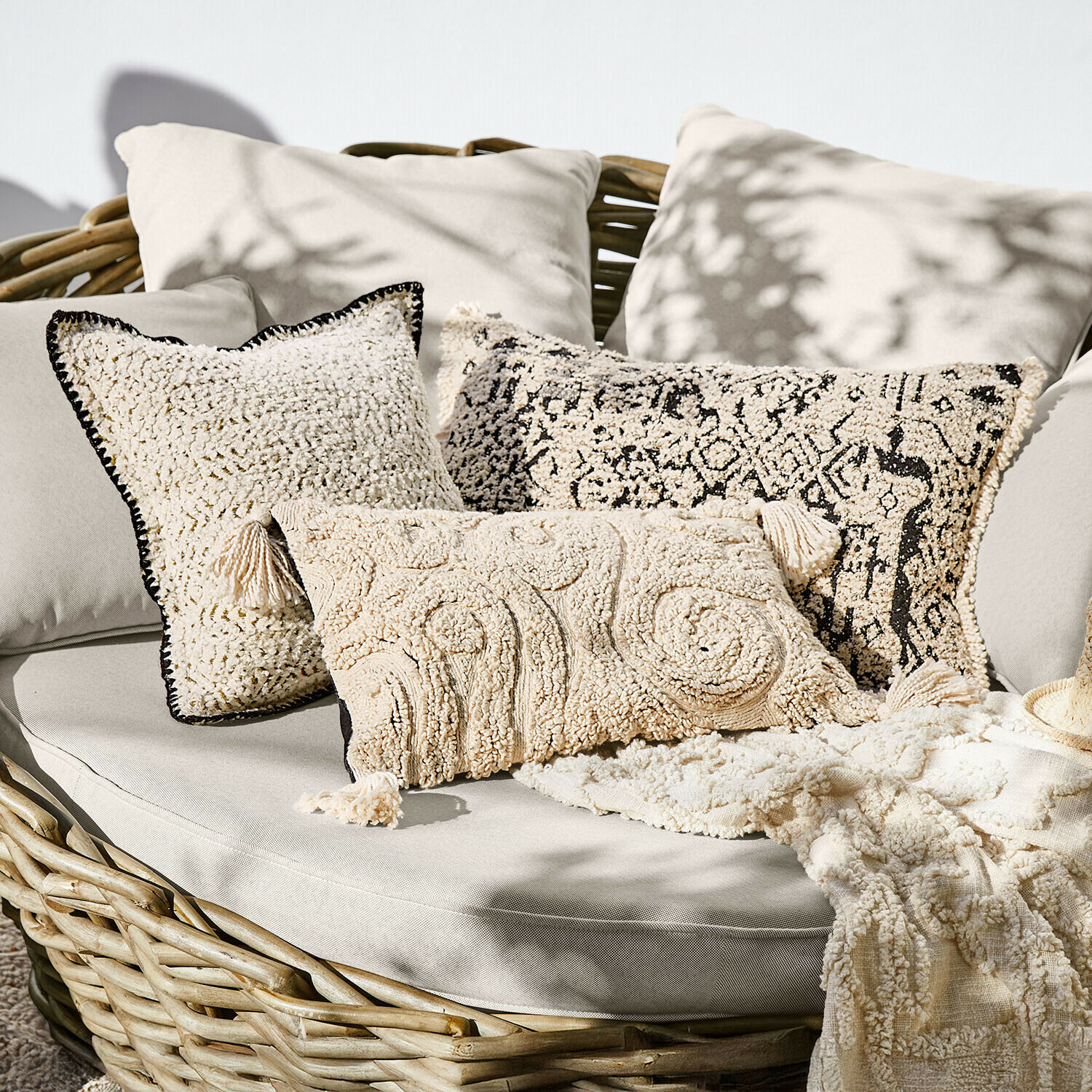 Set aus cremefarbenen Dekokissen aus weichem Material auf Rattansofa, Boho-Stil